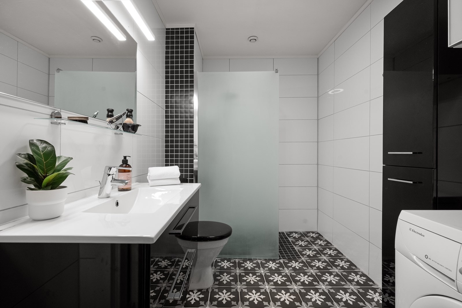 Badet er innredet med dusj, toalett, vask i skuffeinnredning og spieil med belysning. Her er det også satt opp garderobeskap og opplegg for vaskemaskin. Galleribilde