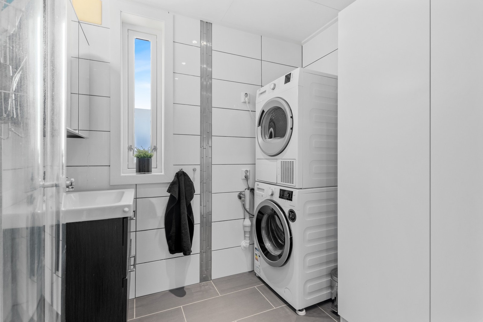 Badet er flislagt og inneholder dusj med glass-dører, wc, servant i innredning og opplegg for vaskemaskin og tørketrommel. Galleribilde