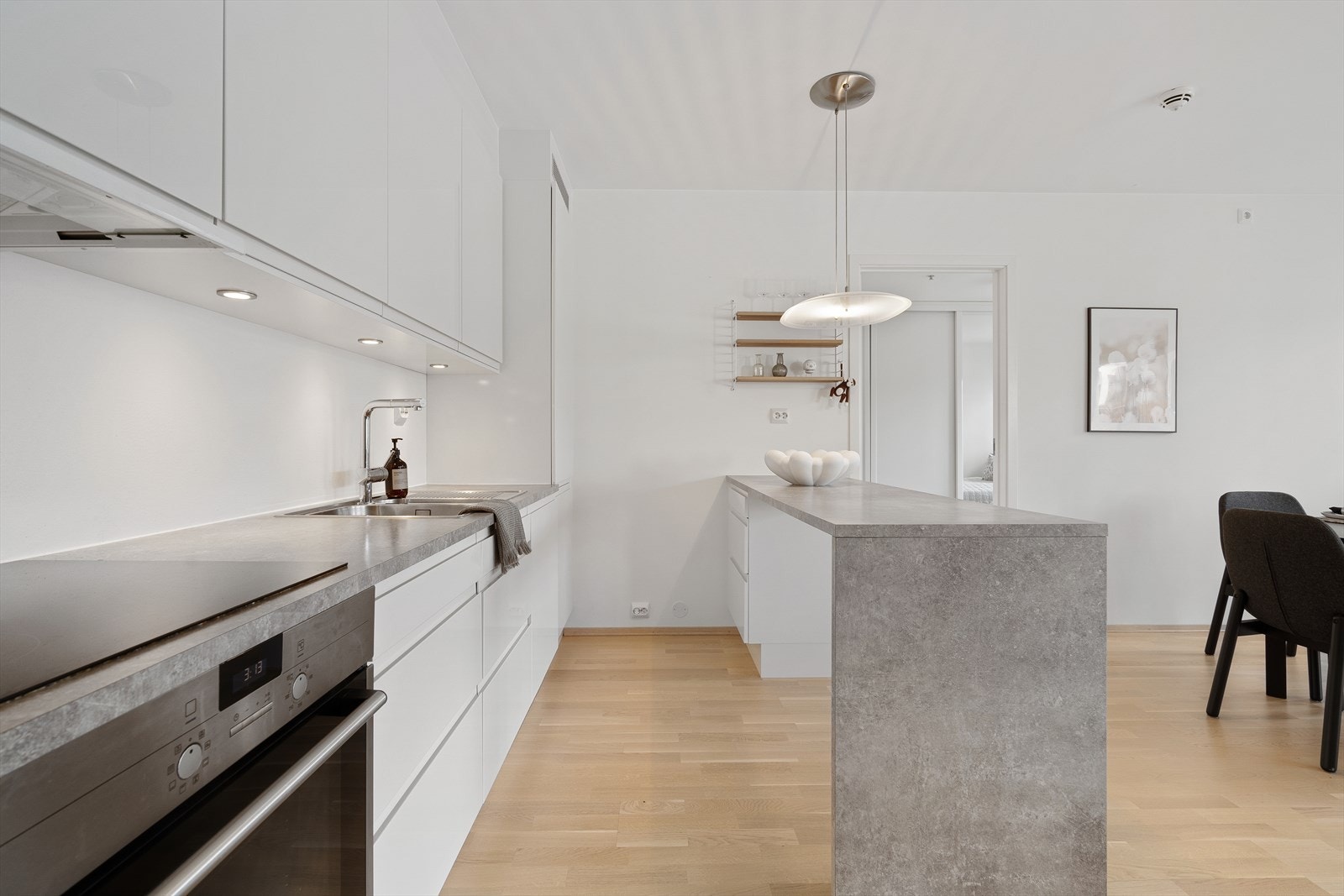 Kjøkkenet i leiligheten er tidsriktig og stilrent med sine slette, hvite fronter og en benkeplate i gråtoner. Galleribilde