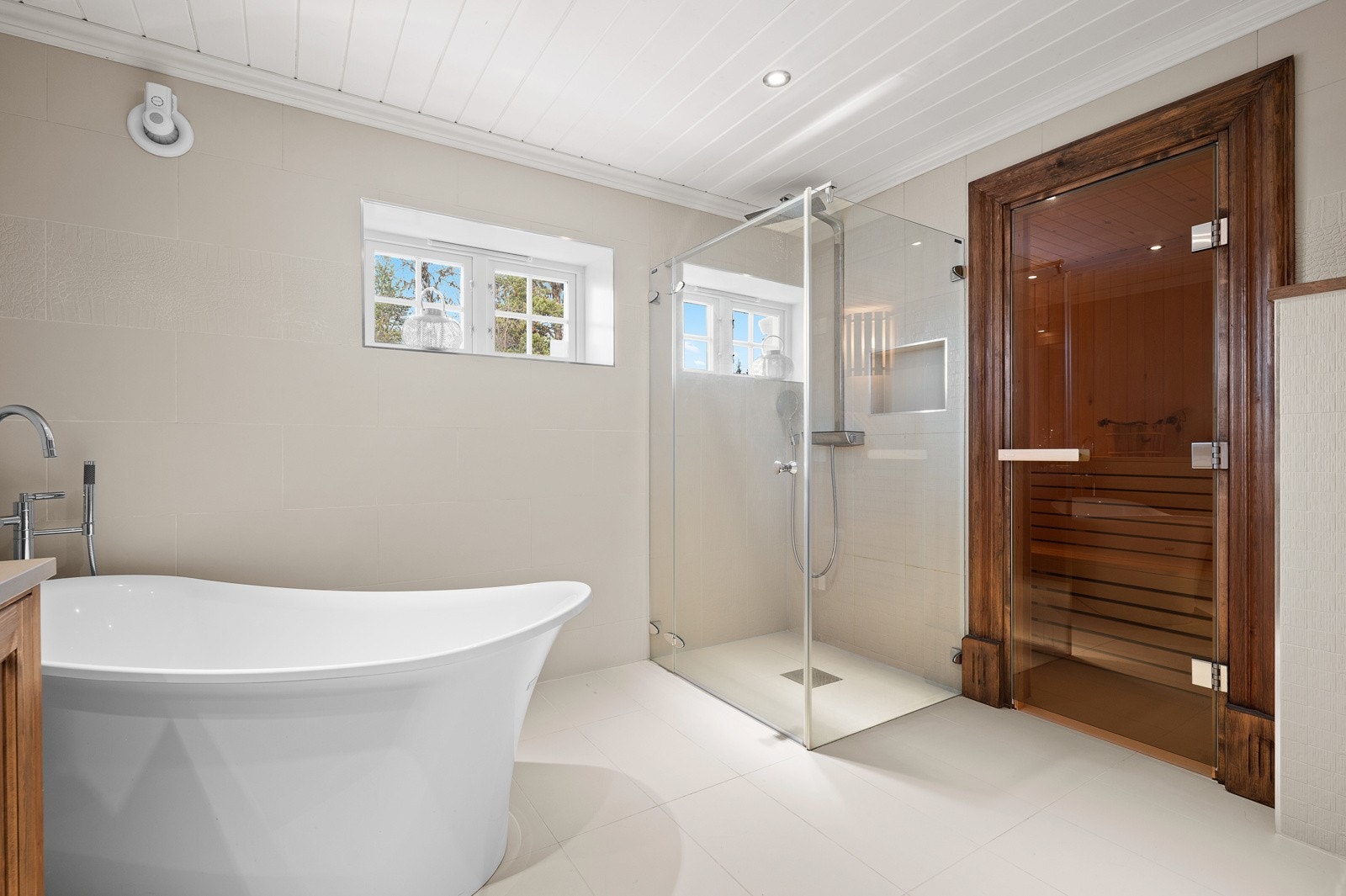 Plassbygget innredning med to toppmonterte servanter, vegghengt toalett, en stor walk-in dusj med waterfall-armatur, badekar og badstue Galleribilde