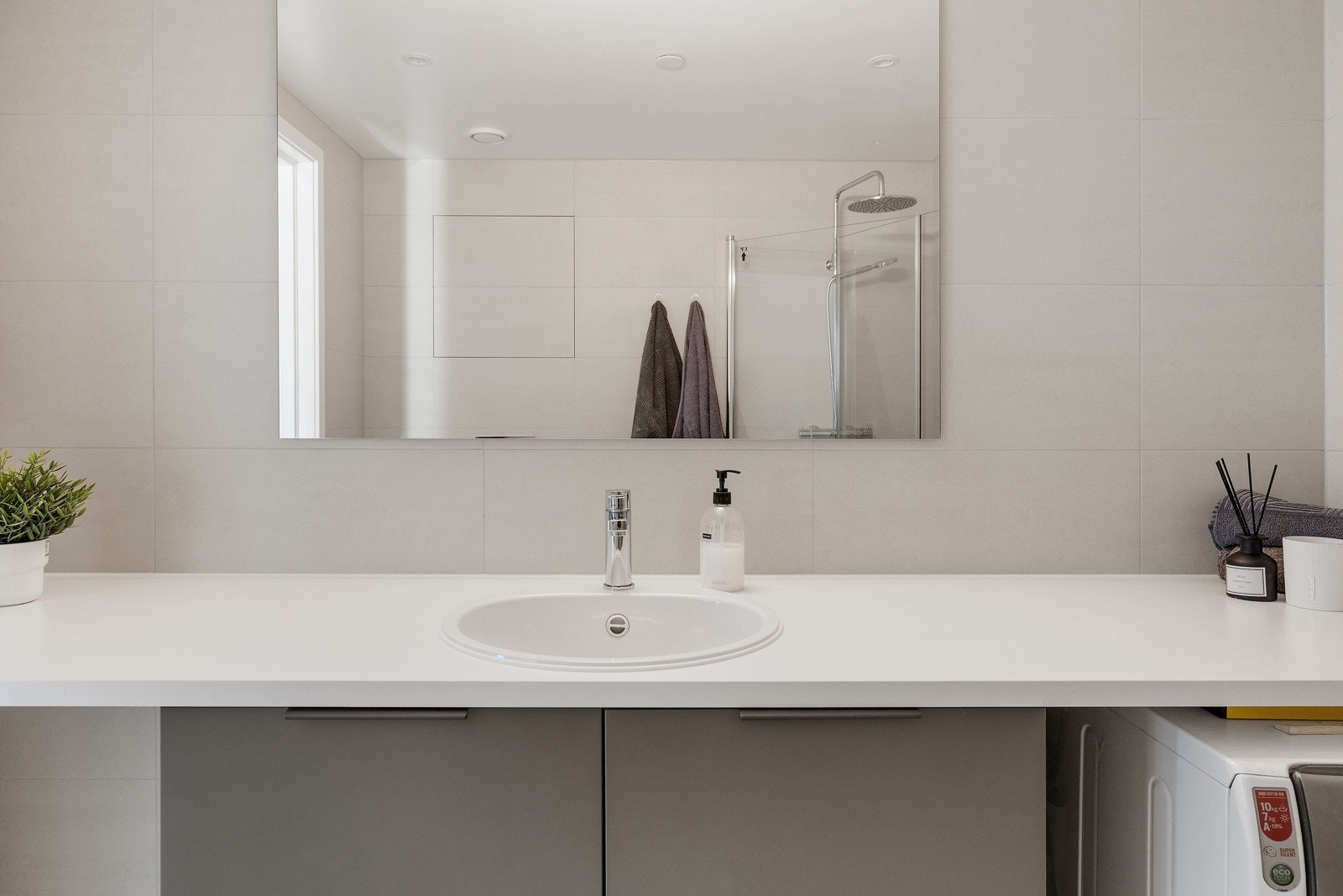 Innredningen består av vegghengt servantskap, speil med overbelysning, dusjhjørne og vegghengt toalett Galleribilde