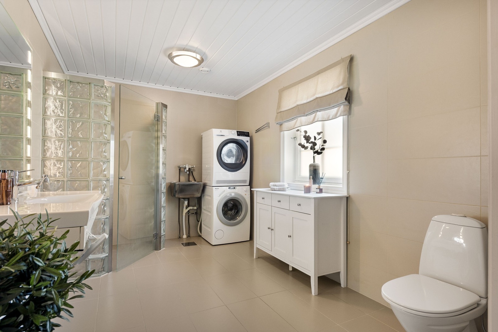 Stort, flislagt baderom med dusj, toalett, vask i innredning og opplegg for vaskemaskin. Galleribilde