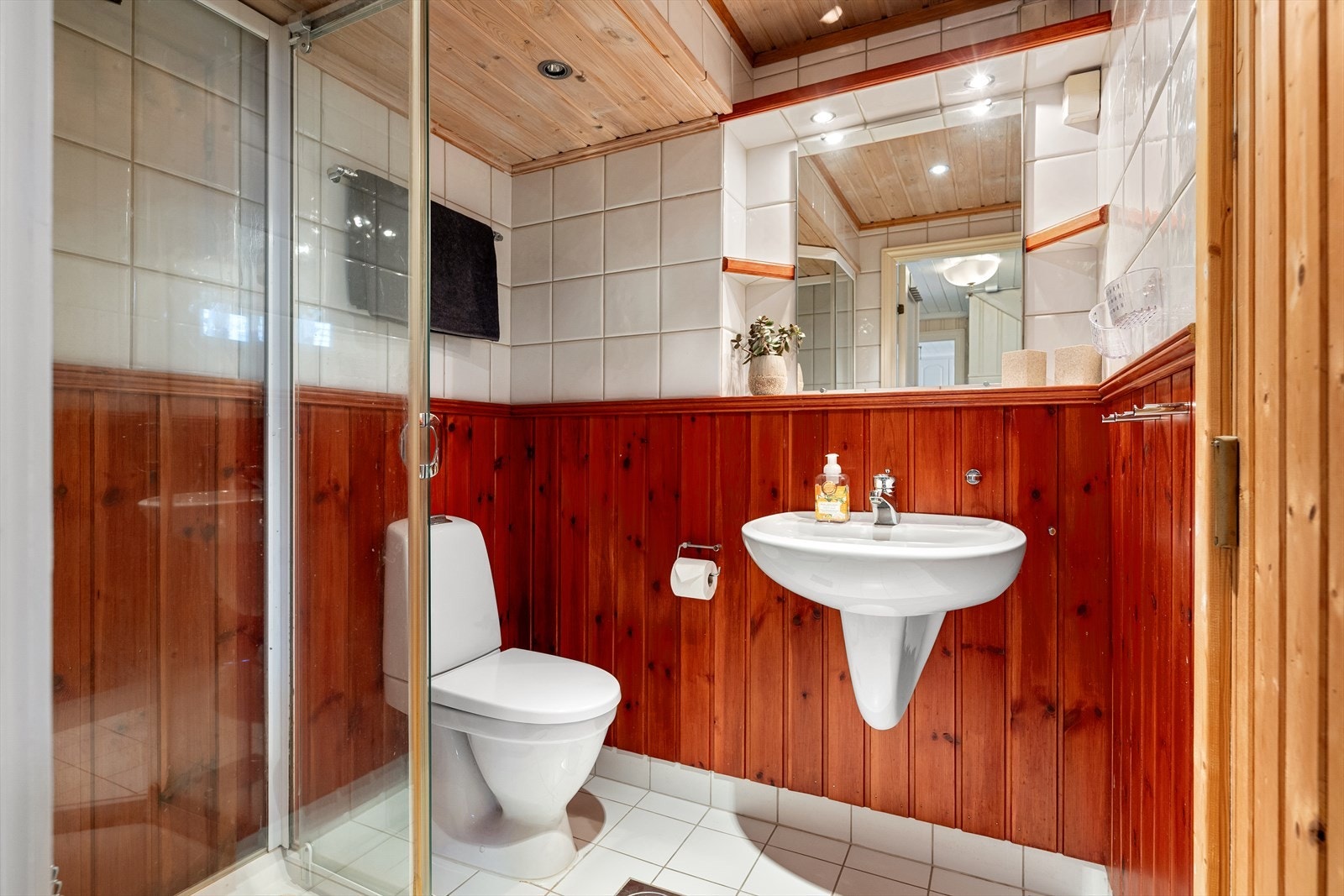 Bad med varmekabler i gulv og adkomst til badstue. Flislagt gulv, og veggene er delvis flislagte og kledd med panel. Baderomsinnredningen består av dusjkabinett, gulvmontert toalett og vegghengt vask. Galleribilde