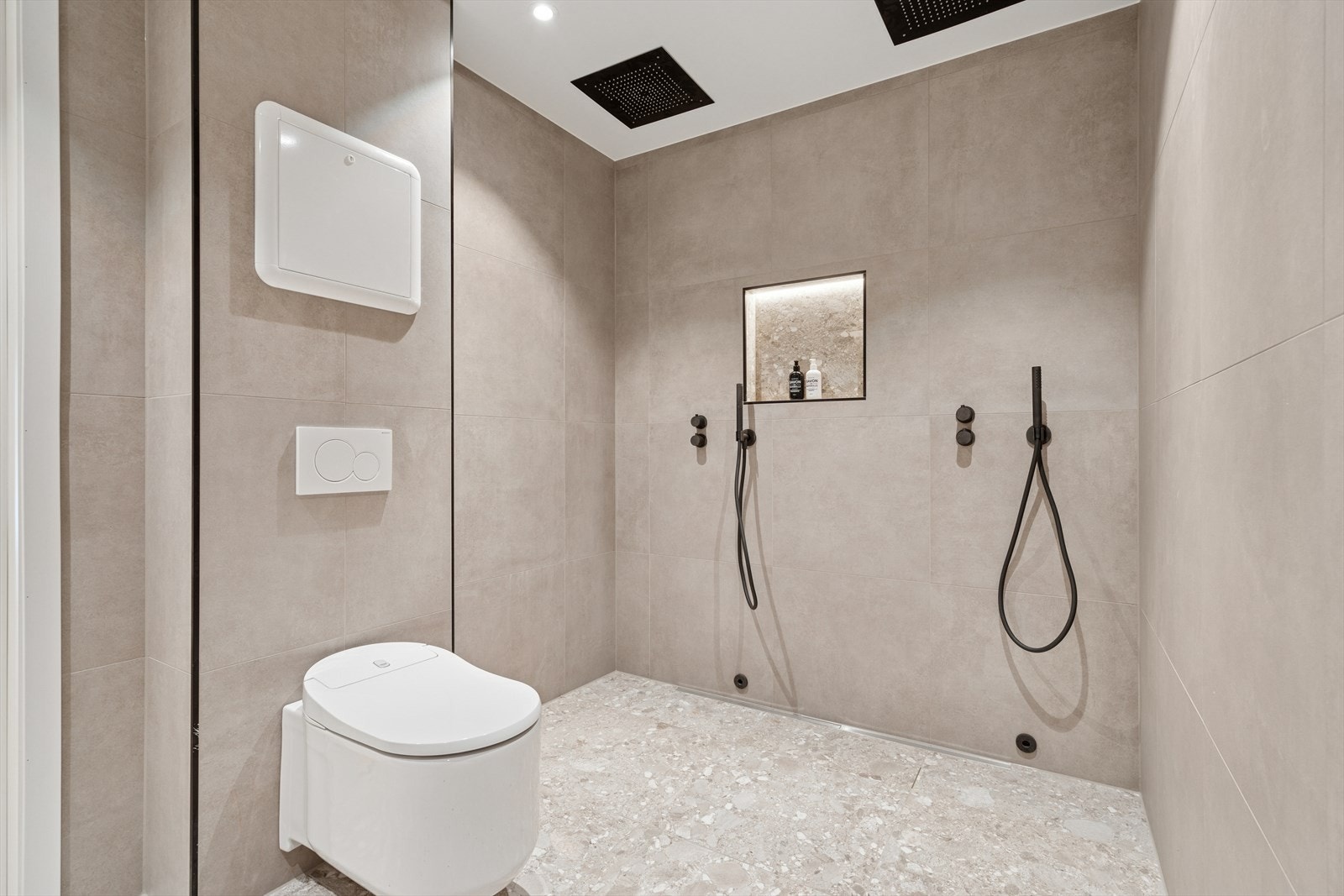 Badet er utført med flislagte overflater - Her finner du vegghengt toalett (elektrisk) og dusjnisje med bl.a. integrerte armaturer, dobbel regnfallsdusj og integrert vegghylle Galleribilde