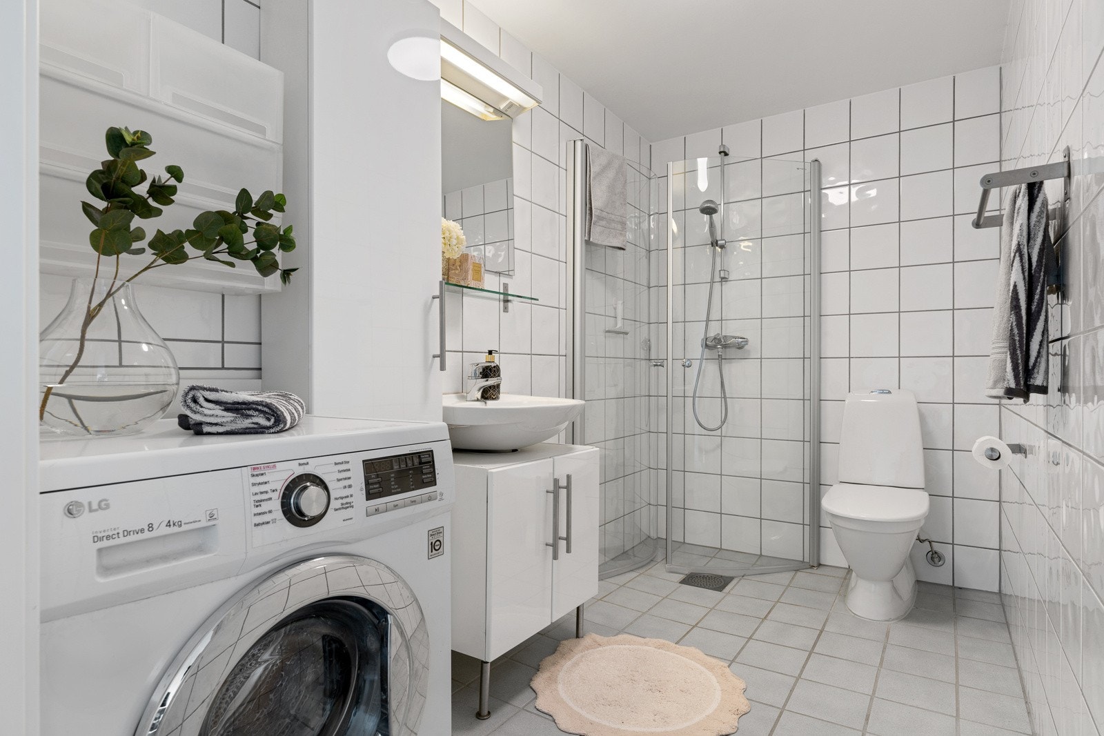 Flislagt baderom med behagelig varme i gulv. Badet er utstyrt med en romslig baderomsinnredning med godt med oppbevaringsplass, dusjhjørne med innfellbare dører, toalett og opplegg for vaskemaskin. Galleribilde