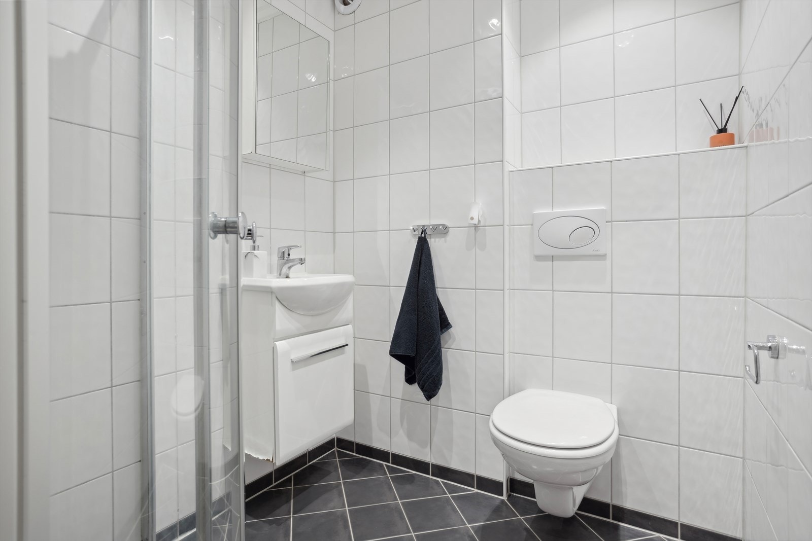 Baderomsinnredning består av servant med speilskap, vegghengt toalett, buet dusjhjørne i glass med innfellbare dusjdører. Avtrekksventil i vegg. Galleribilde