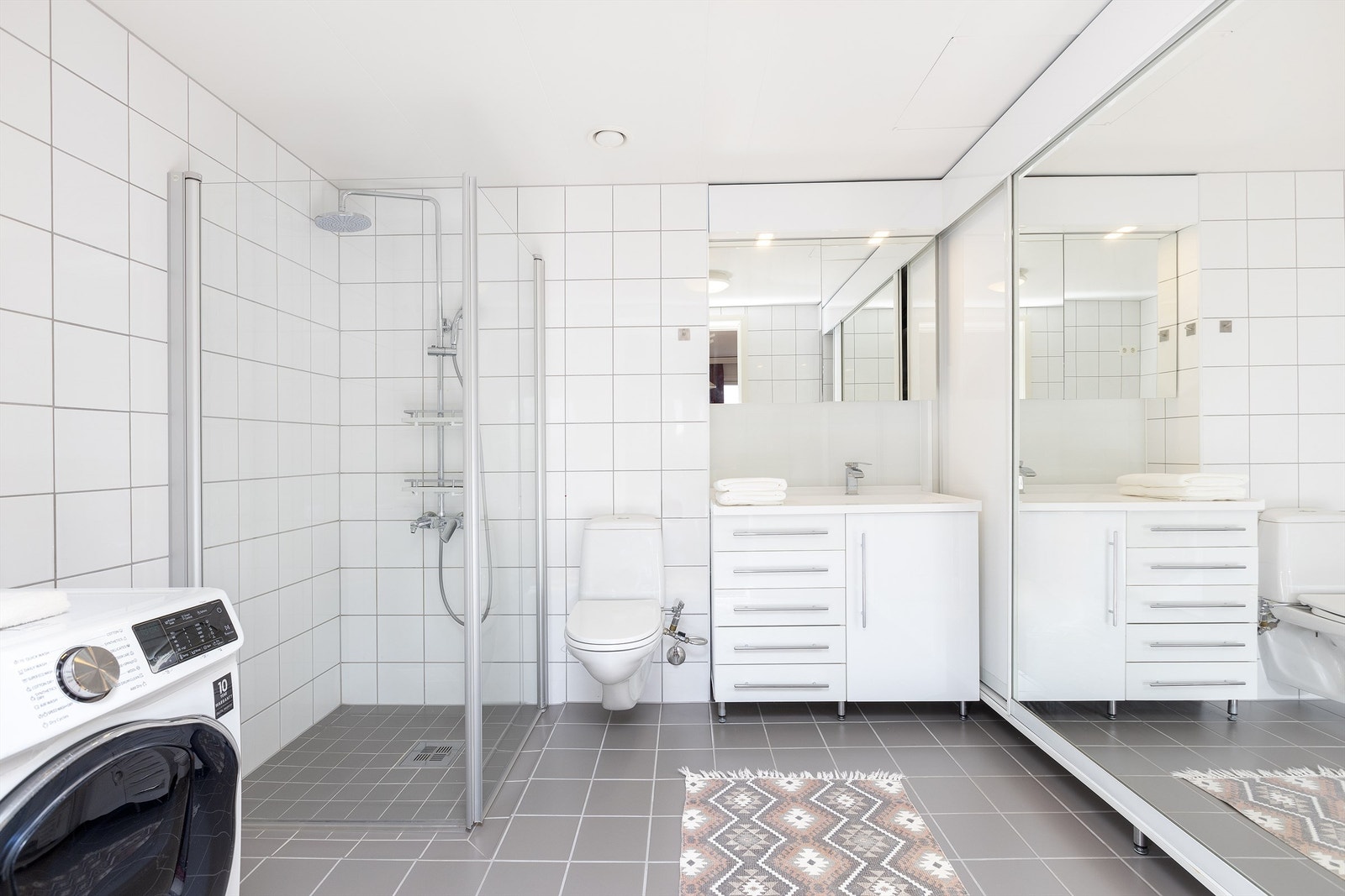 Badet består av vegghengt servantskap, speilskap over servant med overlys, dusjnisje med innfellbare glassdører og dusjarmatur, samt vegghengt toalett Galleribilde
