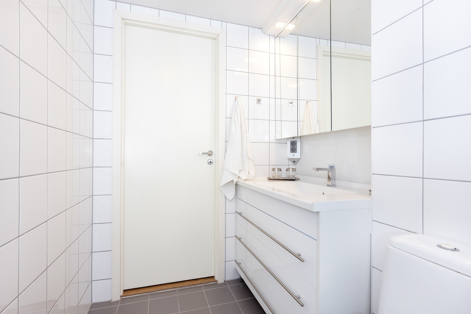 Badet består av vegghengt servantskap med heldekkende servant, speilskap over servant med overlys, dusjnisje med innfellbare glassdører og dusjarmatur, samt vegghengt toalett Galleribilde