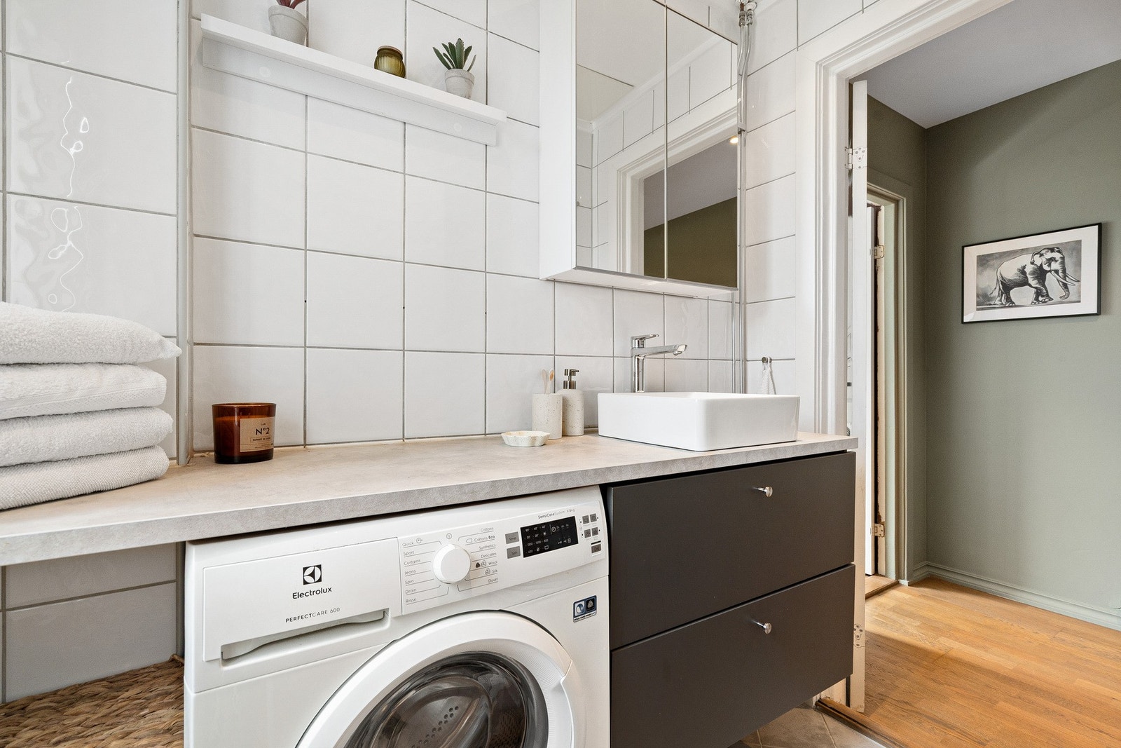 Badet består av laminert benkeplate med servant, speilskap, gulvmontert toalett og innfellbare dusjdører i herdet glass. Galleribilde