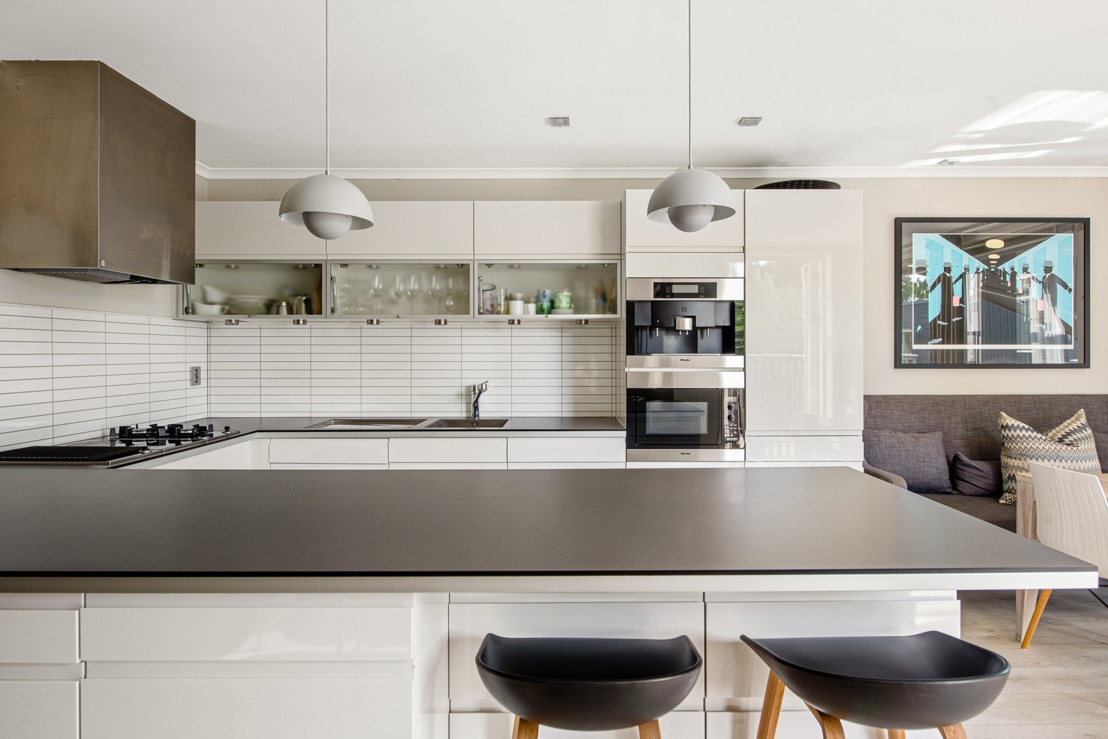 Benkeplatene er i sort laminat og har stålkant. Nedfelt i benken er det oppvaskkum med avrenningsfelt og koketopp med både induksjonstopp og gassbluss. Over koketopp og vask er det avtrekk fra ventilator, benkebelysning og hvite fliser på veggene bak. Galleribilde