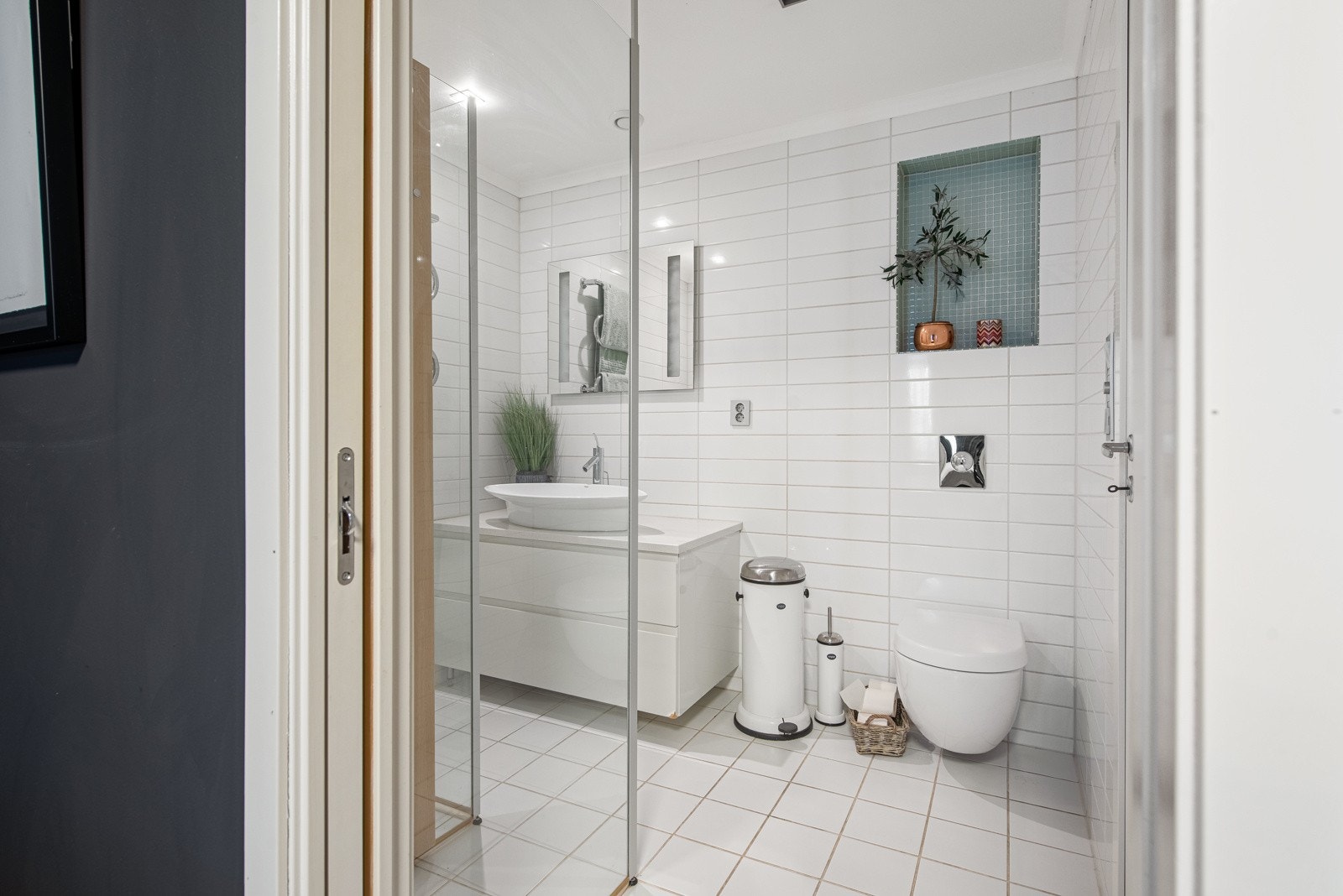 Baderommet i andre etasje har dør inn fra gangen og også direkte adkomst til hovedsoverommet via en skyvedør. Vegg- og gulvflater er dekket med hvite fliser i to ulike størrelser, og over vegghengt toalett er det en nisje med grønne mosaikkfliser. Galleribilde