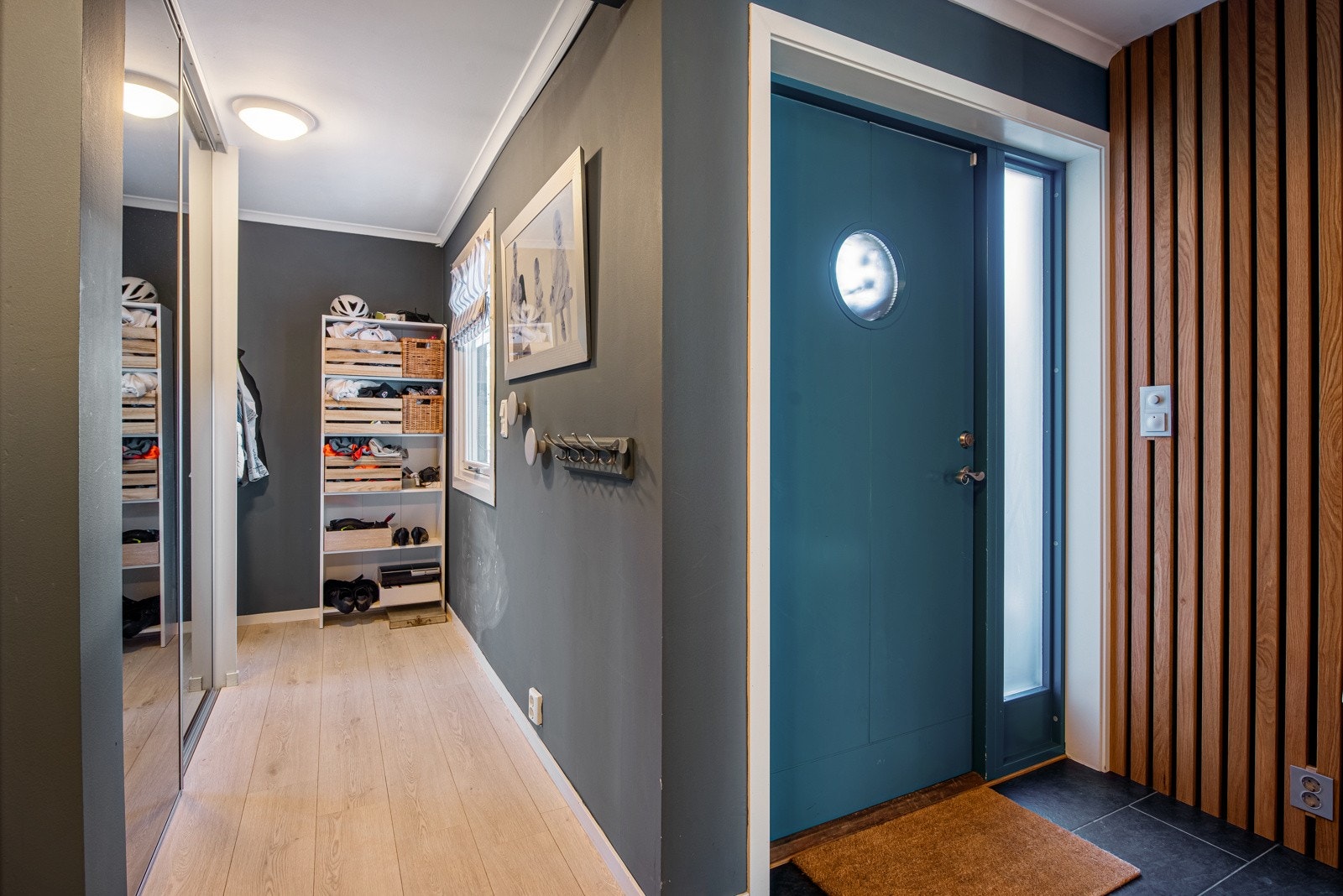 I den tilbygde delen av entreen er det enstavs laminatgulv, gulvvarme og gråmalte vegger. Et vindu gir fine lysforhold og en romslig skyvedørsgarderobe med speilfronter bidrar til god oppbevaringsplass til yttertøy, sko og annet utstyr. Galleribilde