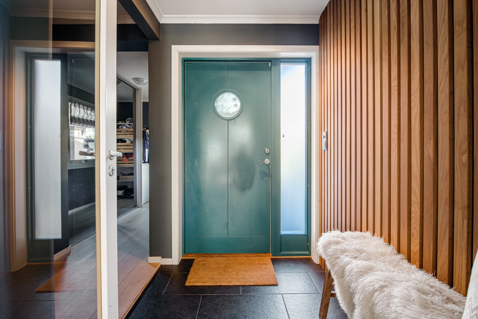 I entreen er det sorte gulvfliser med gulvvarme, gråmalte vegger, en spilevegg og glassdør inn til stuen. Galleribilde