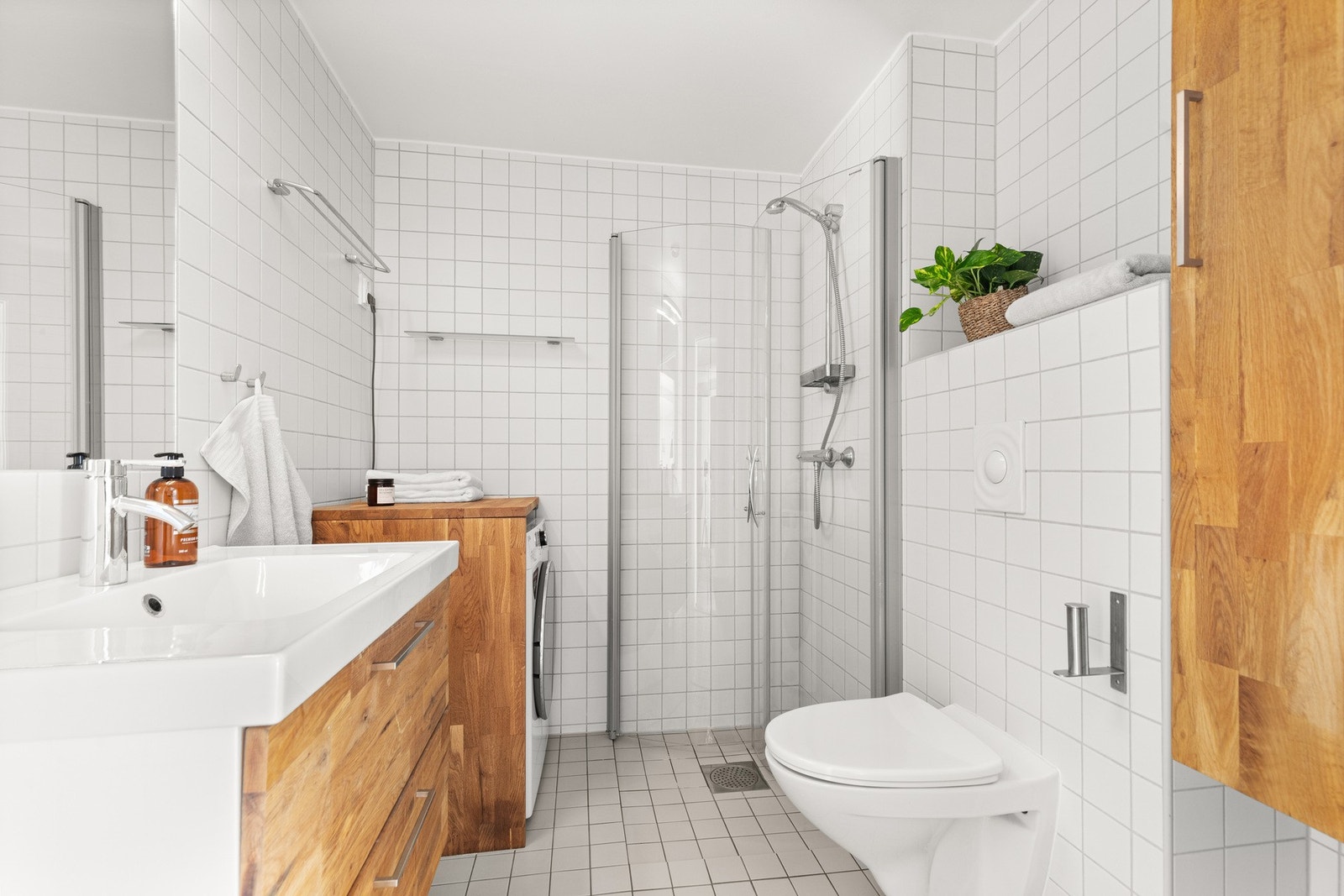 Badet er utstyrt med dusj med glassvegger, servantseksjon med skuffer og vask, innmurt speil med lys, veggskap, wc og opplegg for vaskemaskin. Galleribilde