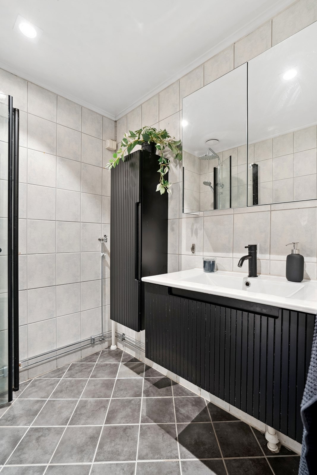 Badet er blant annet utstyrt med et gulvstående toalett, et dusjhjørne med svingbare glassdører, og en servant med skuff under. Galleribilde