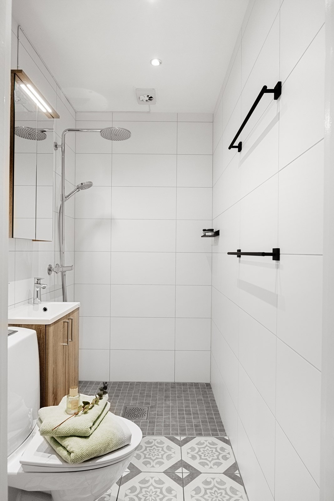 Badet er innredet med servantskap med nedfelt servant, veggskap med speildører og lys, gulvmontert toalett og dusjsone med dusjforheng. Galleribilde