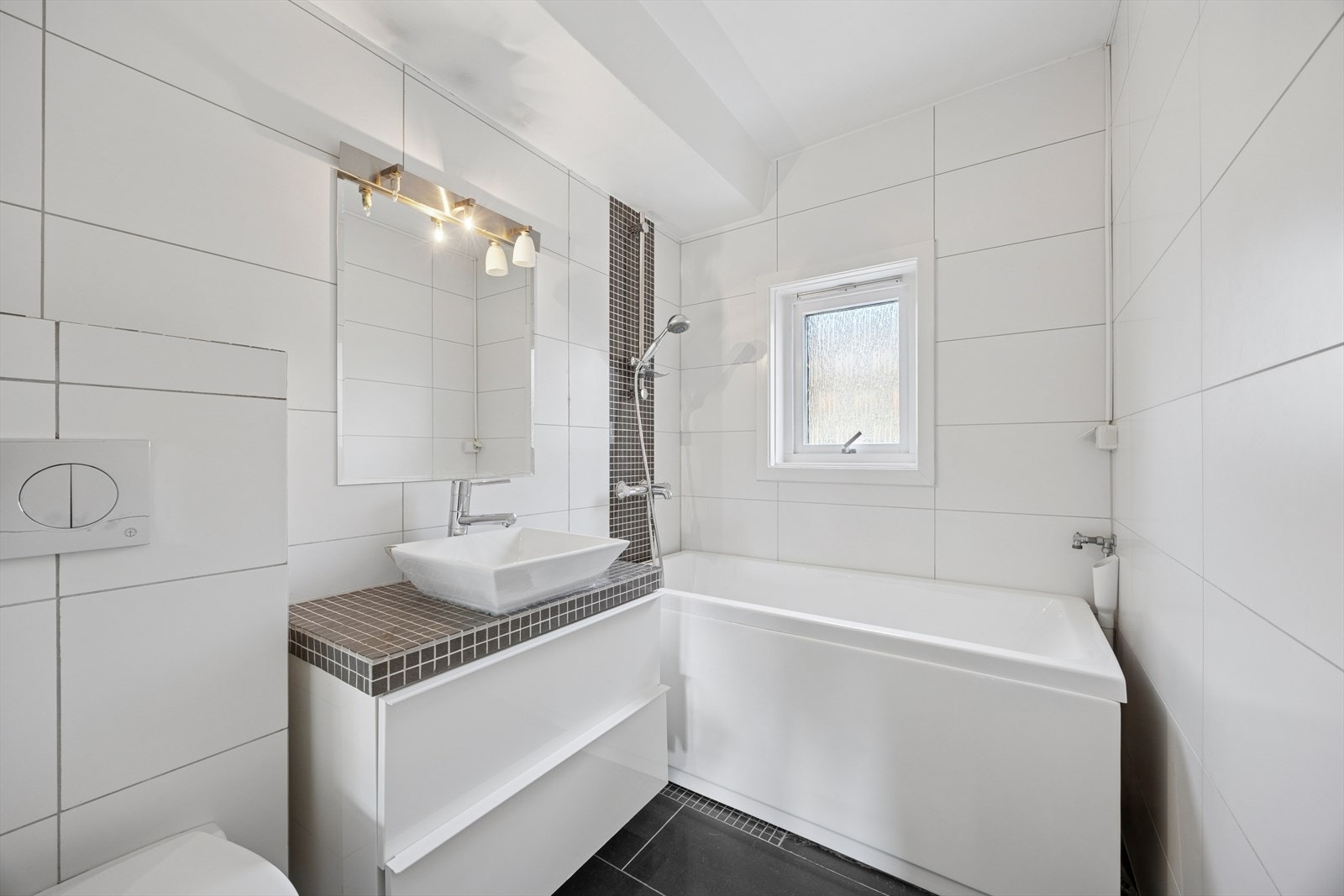 Badet er innredet med frittstående servant, vegghengt toalett og badekar, samt praktisk opplegg for vaskemaskin. Galleribilde