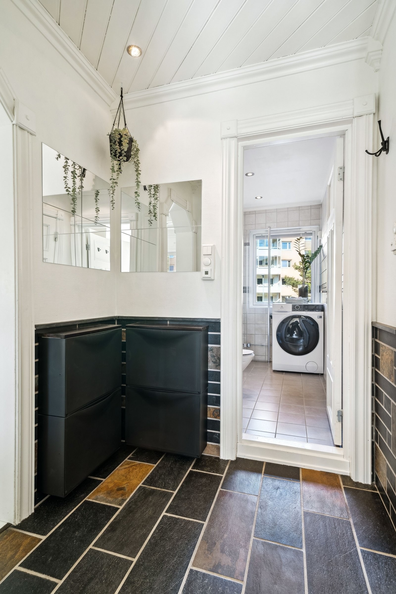 Gang med skiferfliser og varmekabler i gulv. Lysmalte vegger, downligts i tak og innebygd skap for oppbevaring. Galleribilde