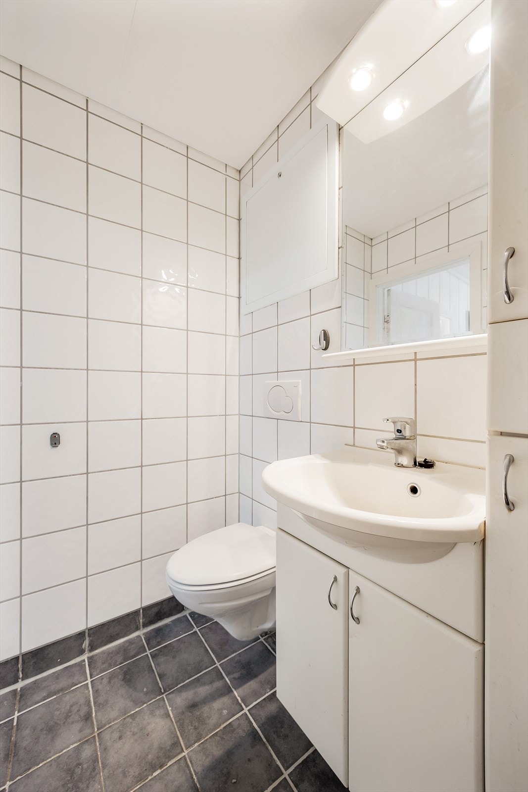 Videre er det vegghengt toalett, servant med underskap, speil, og veggskap. I gulvet er det lagt varmekabler. Galleribilde