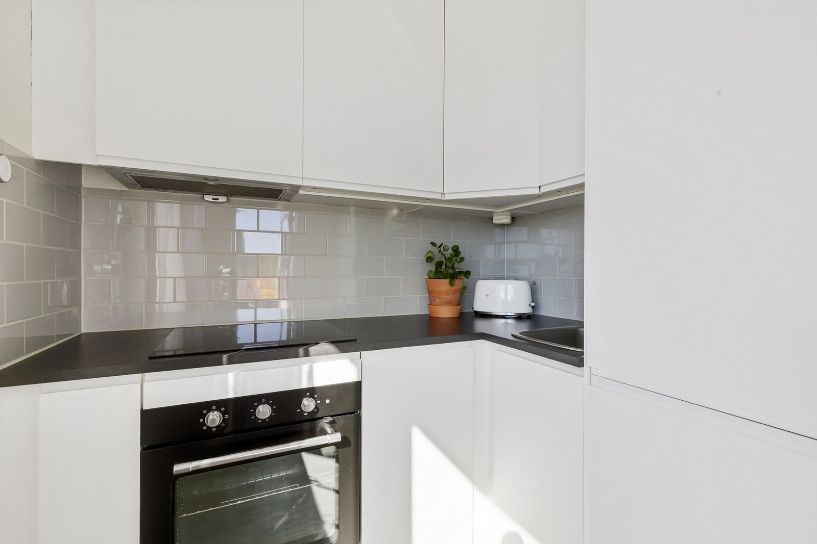 Stilrent kjøkken med integrerte hvitevarer som komfyr, platetopp, oppvaskmaskin og kjøleskap med frysedel. Galleribilde