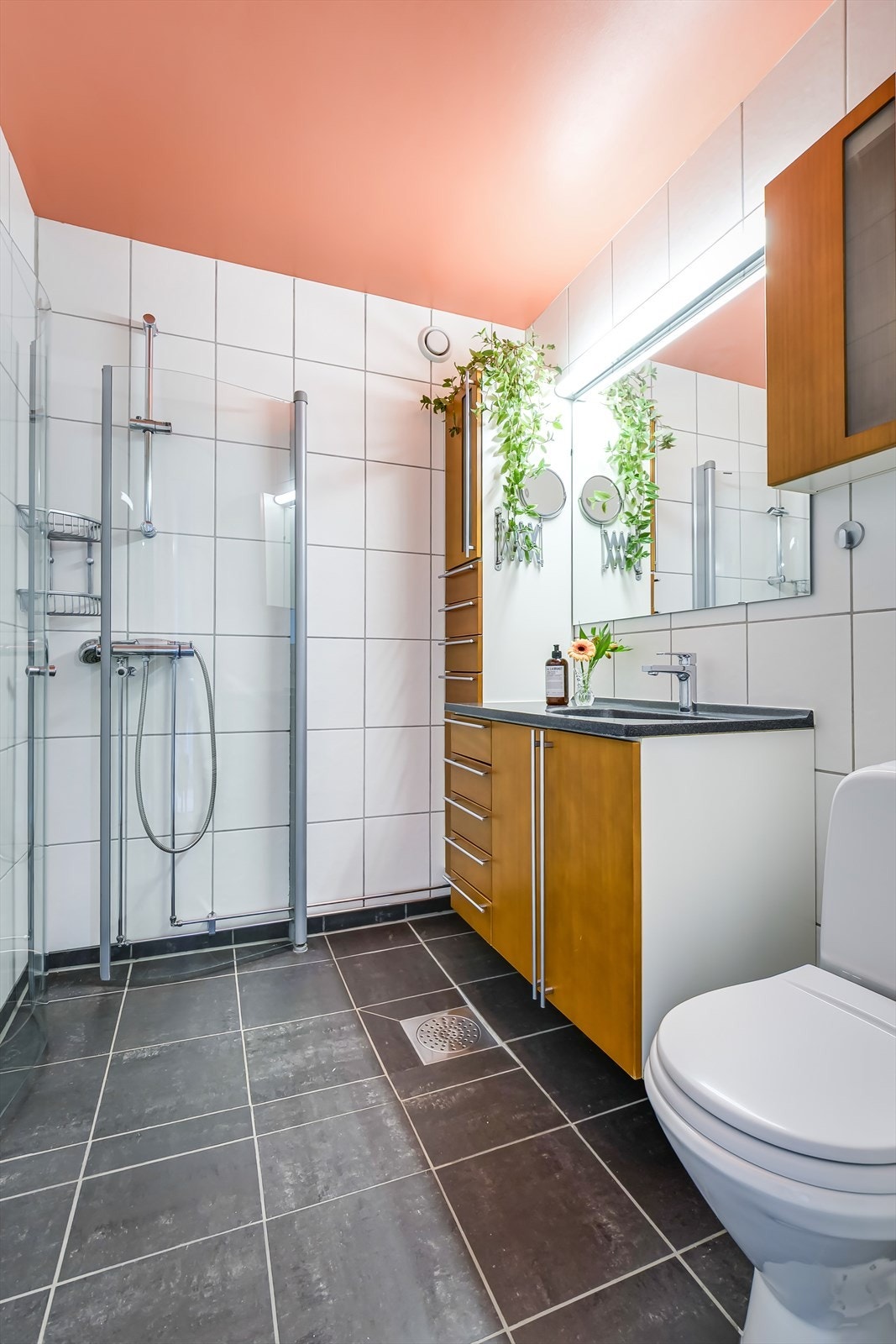 Badet er innredet med dusjhjørne med svingbare glassdører, frittstående toalett, servant med underskap, speil med lys over og og skap for oppbevaring. Galleribilde