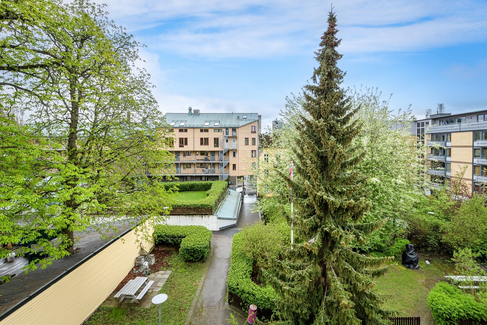 Utsynet fra balkongen viser en pent opparbeidet og frodig bakgård. Galleribilde