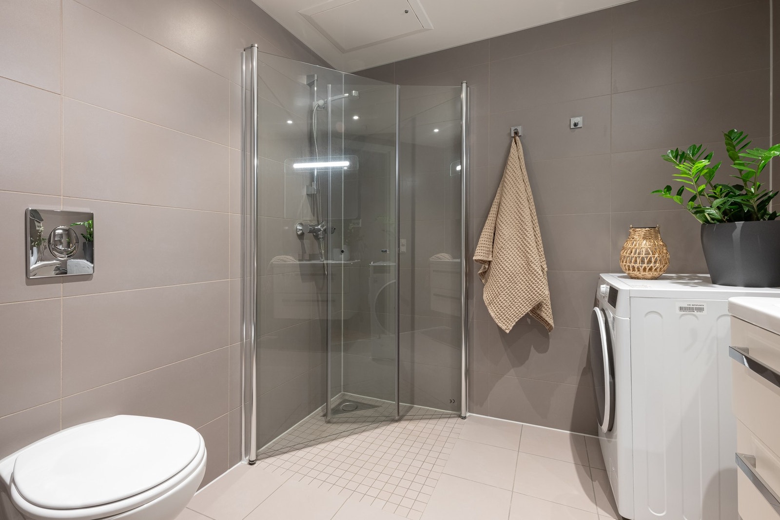 Videre er det dusjhjørne med innfellbare glassdører og vegghengt toalett. Badet har opplegg for vaskemaskin. Galleribilde