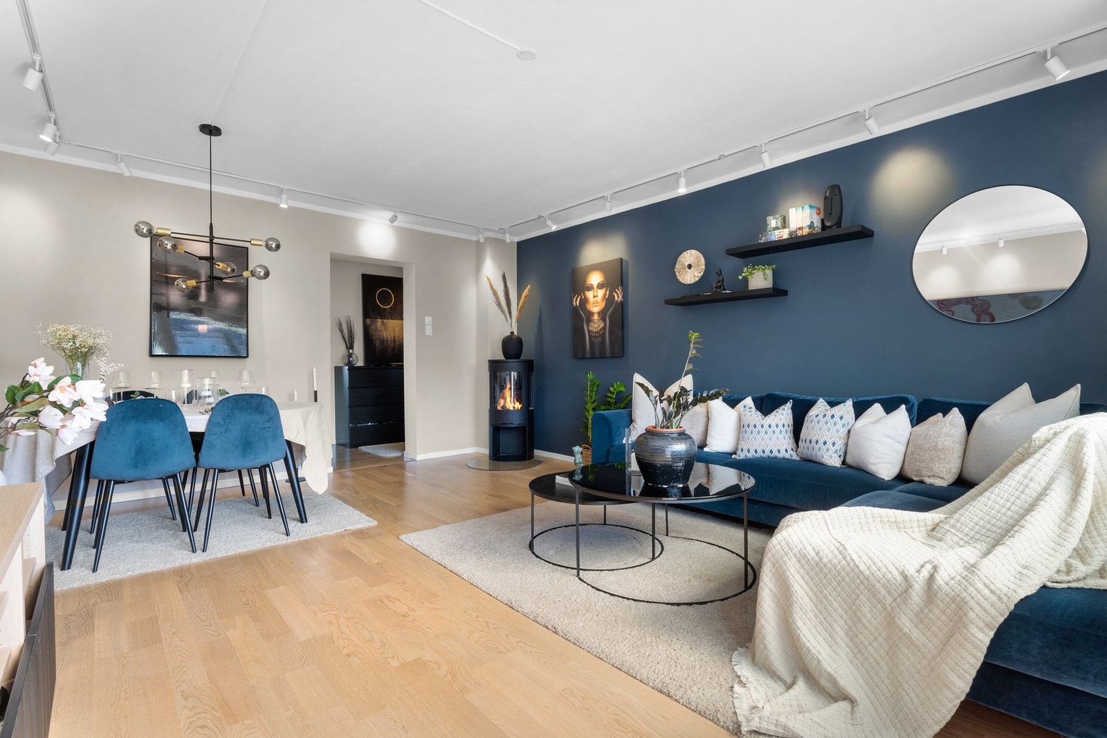 Pen og romslig stue med slette vegger malt i lyse farger og på en av langsidene er det malt en mørk blåfarge som skaper en god kontrast til resten av rommet. Galleribilde