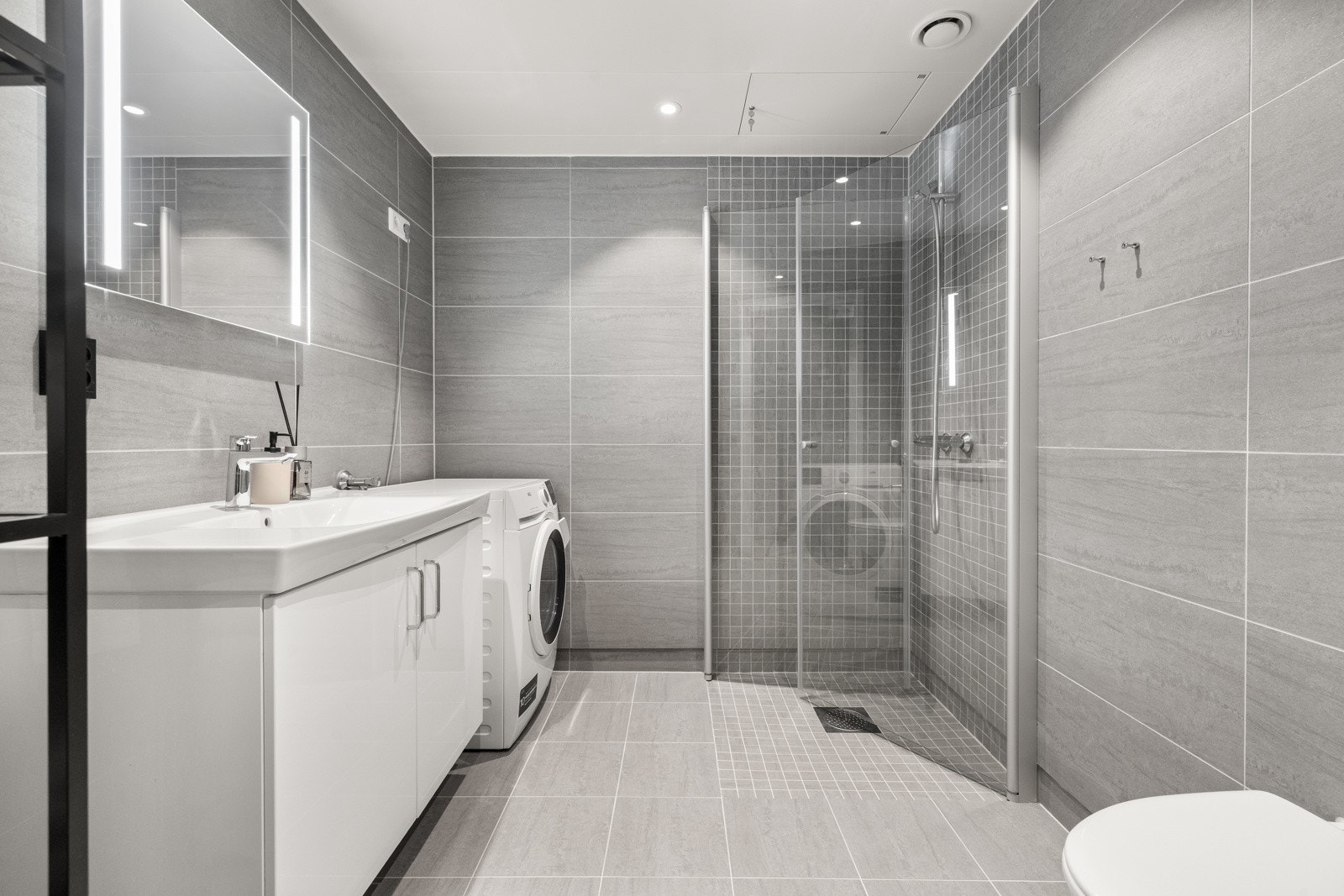 Romslig og delikat baderom med flislagte overflater, gulvvarme og opplegg for vaskemaskin. Galleribilde