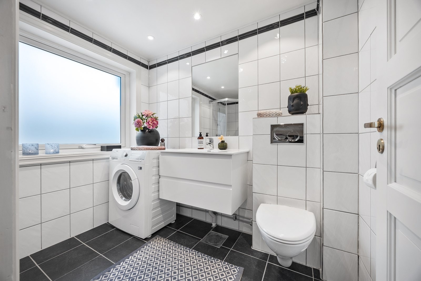Pent flislagt bad fra 2002, med varmekabler i gulvet og downlights i himlingen. Det er opplegg og plass til vaskemaskin. Det informeres om at kombimaskinen (vask/tørk) fra AEG medfølger boligen ved overtakelse. Galleribilde