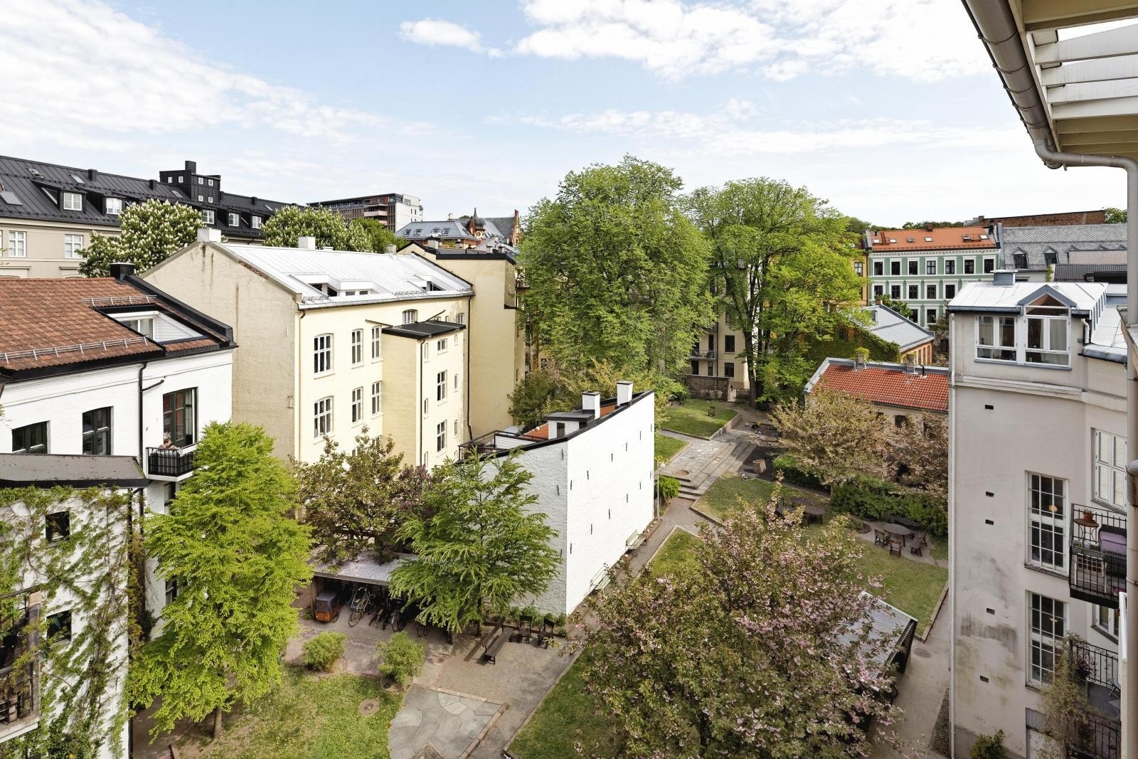 Utsikt over avlukket bakgård fra felles takterrasse. Bakgården har gressplen, hyggelig beplantning, lekeområder, internveier, sykkelparkering m.m. Galleribilde