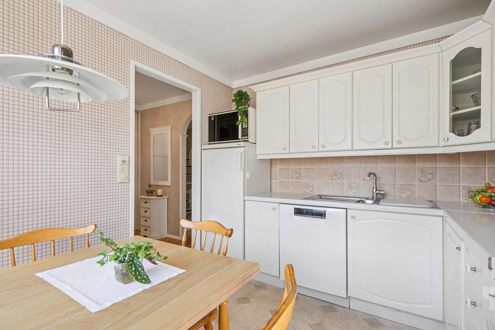 Kjøkkeninnredning med hvite, profilerte fronter og laminert benkeplate med fliser pa vegg over benkeplaten. Galleribilde