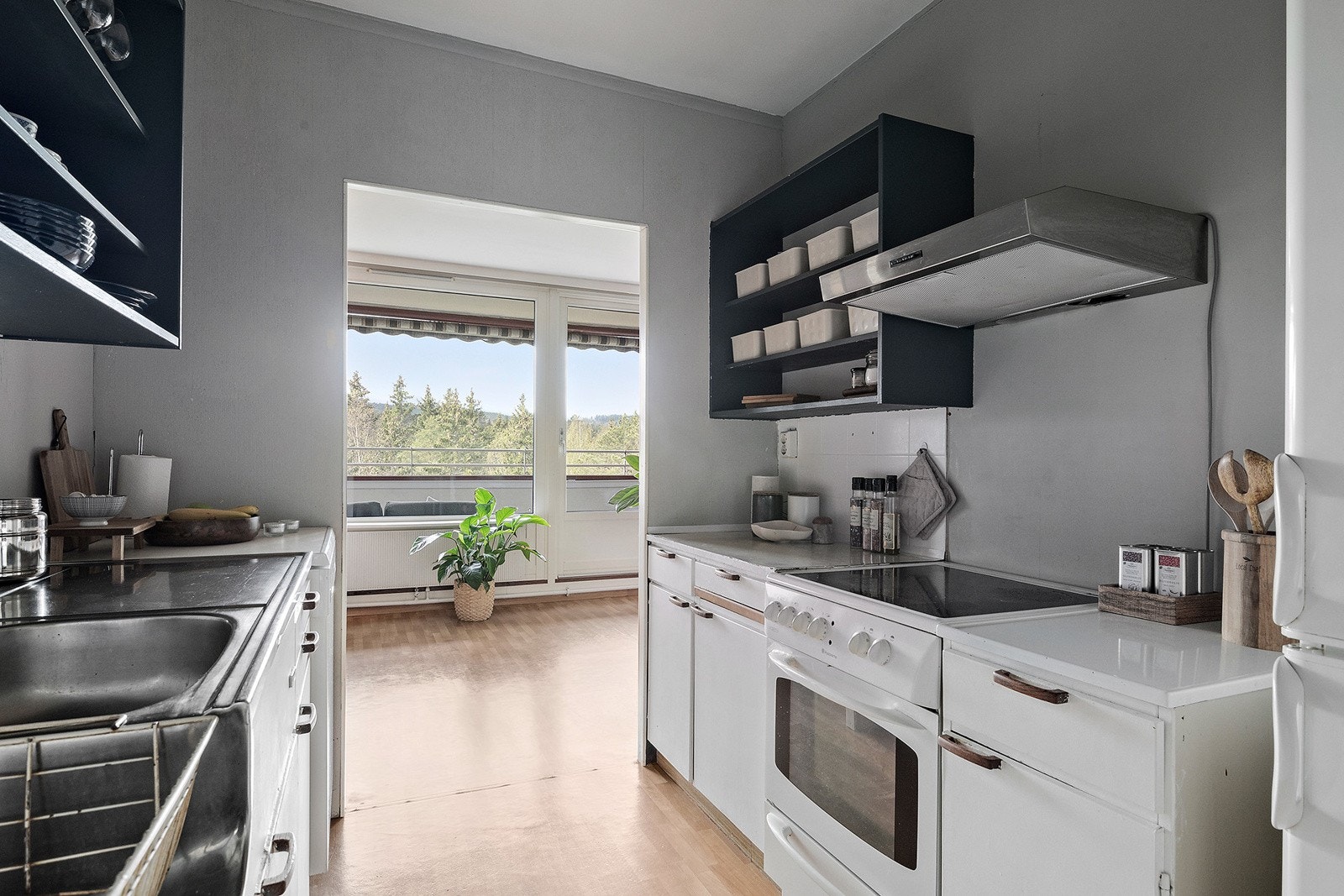 Kjøkkeninnredning med slette, hvite fronter og fliser over laminert benkeplate. Det er lys under overskapene. Det er opplegg for oppvaskmaskin på kjøkkenet. Galleribilde
