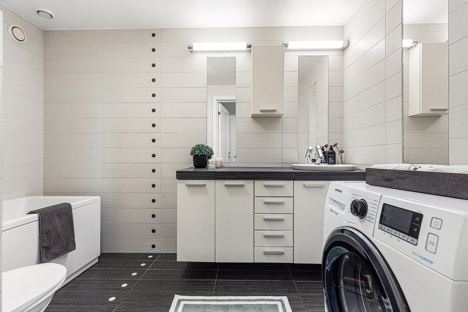 Bad2 med vegghengt wc, badekar, opplegg for vaskemaskin og romslig baderomsinnredning. Galleribilde