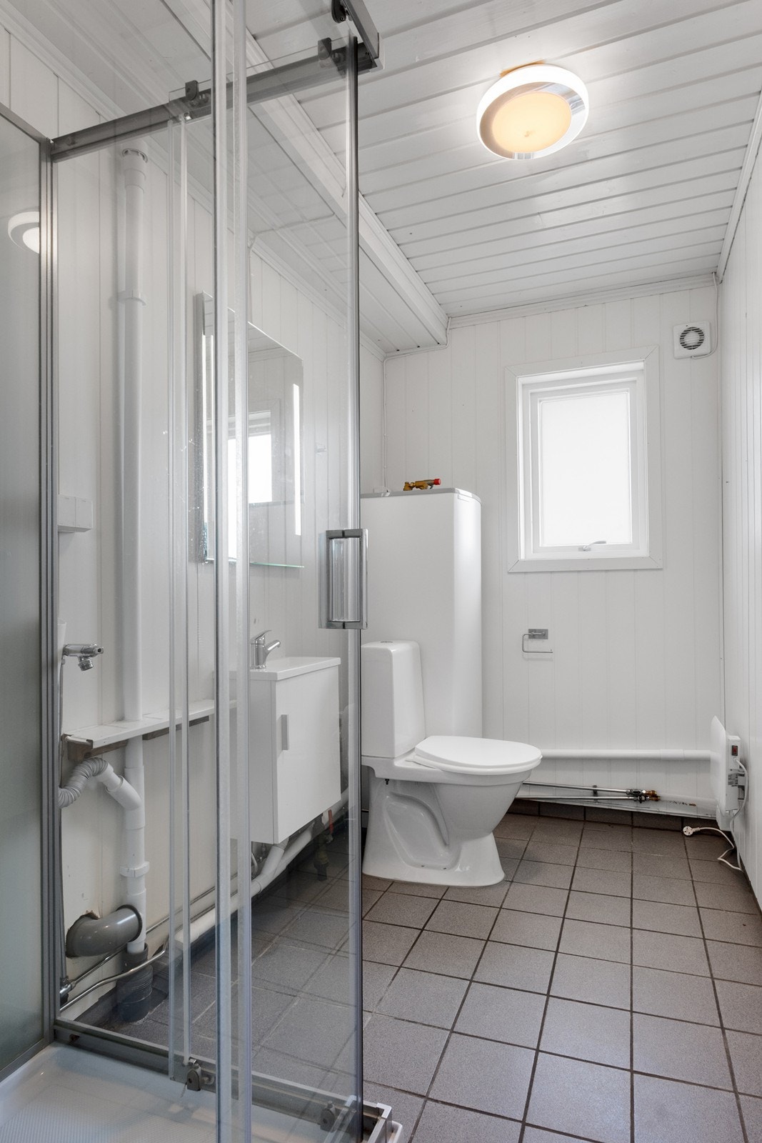 Badet er fra antatt 1980 med flislagt gulv. Innredningen er fra 20/21 og består av dusjkabinett, toalett og enkelt servantskap. Galleribilde