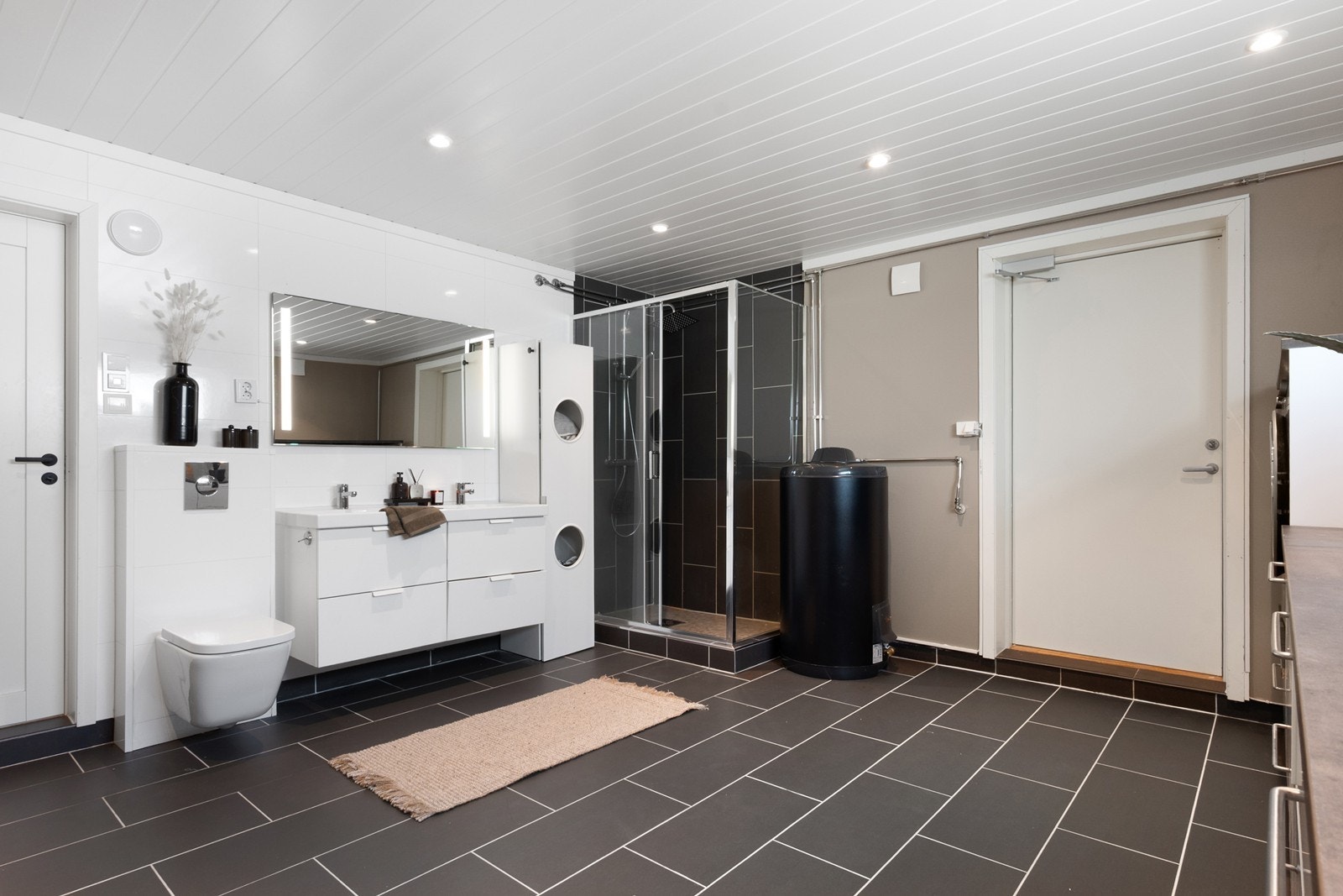 Badet har meget god størrelse og er et flott kombinert bad og vaskerom med flislagt gulv, varmekabler og downlights. Galleribilde