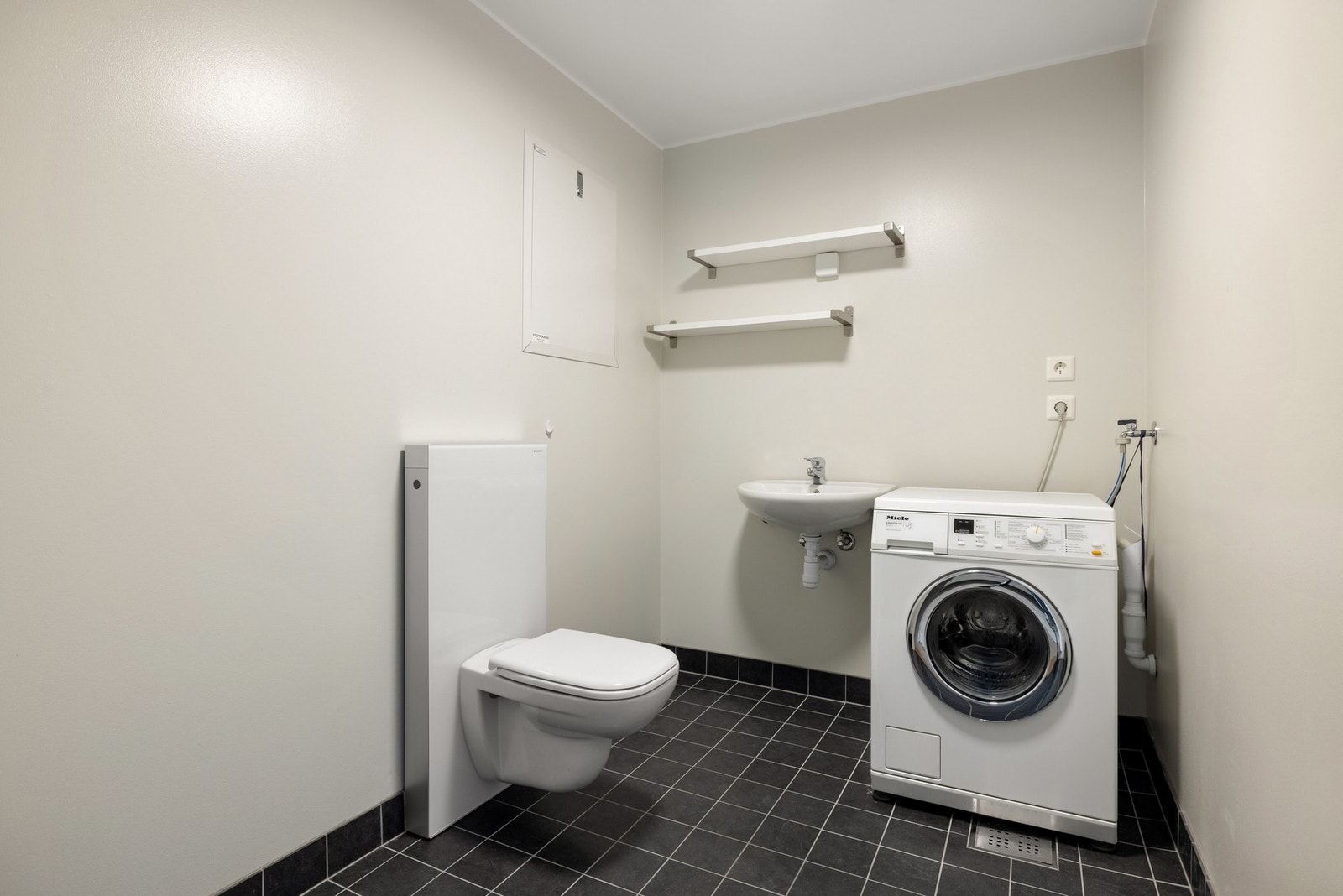 Separat vaskerom med flislagt gulv med varmekabler og malte flater på vegger. Vaskerommet ligger praktisk plassert ved siden av badet, og inneholder servant, samt opplegg og plass for vaskemaskin. Det er også et eget vegghengt toalett på vaskerommet. Galleribilde