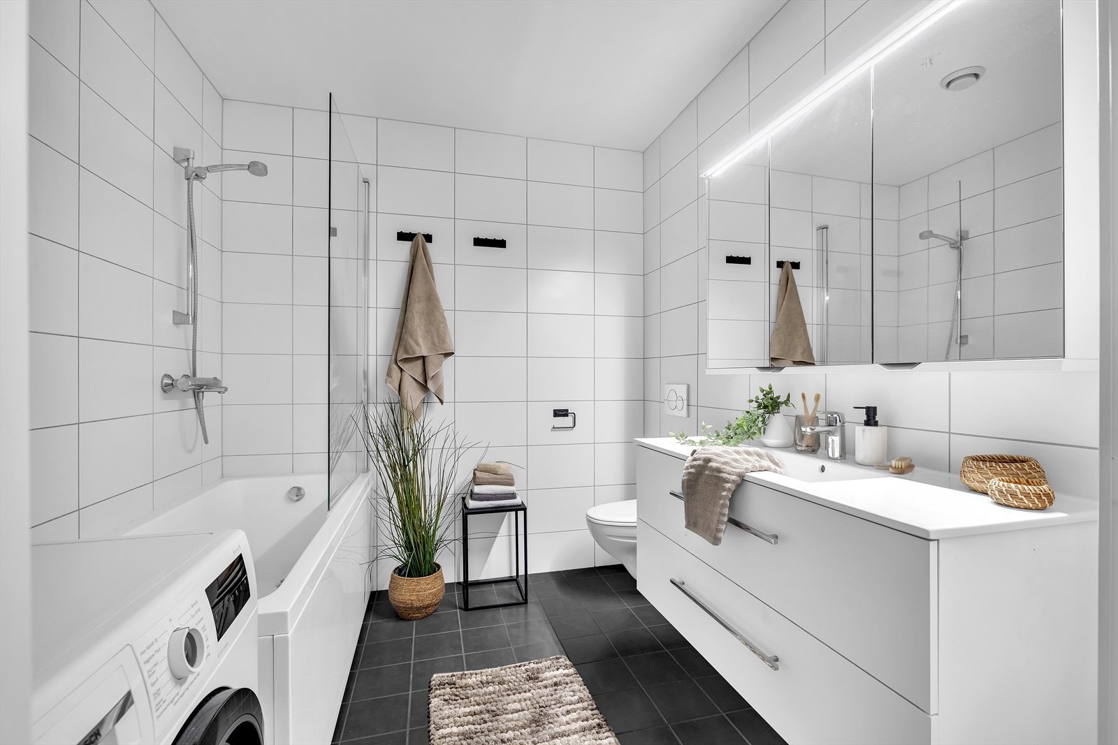 Innbydende, flislagt bad av god størrelse med vegghengt wc, servant med skuffer og dusj i badekar. Galleribilde