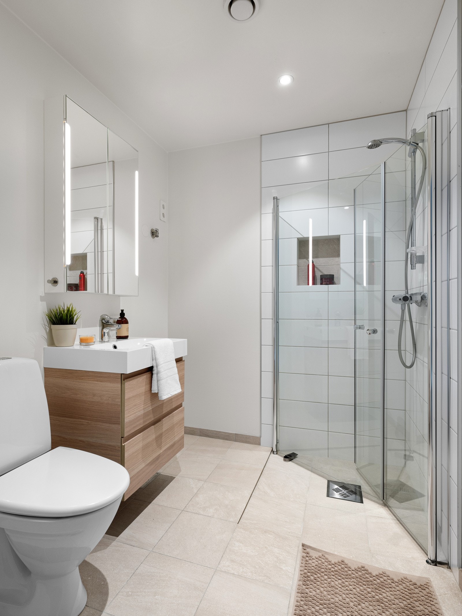 Bad 2 av 2 - Fliser på gulv og i dusjsone. Toalett, servant i skuffeseksjon og dusj med glassdører som kan foldes mot vegg. Det er opplegg til vaskemaskin. Galleribilde