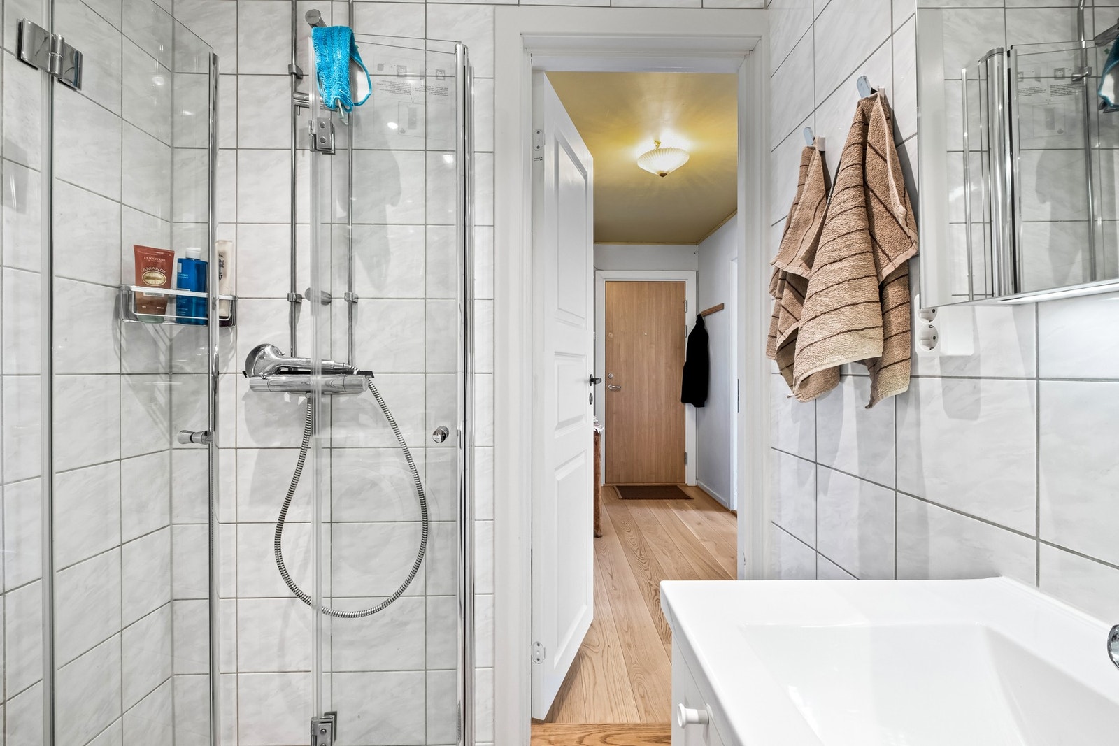 Både badet og wc-rommet har lyse fliser på veggene og grå fliser på gulvet, og badet er i tillegg utstyrt med gulvvarme. På badet er det en hvit skuffeseksjon med heldekkende servant, og over er det et speilskap Galleribilde