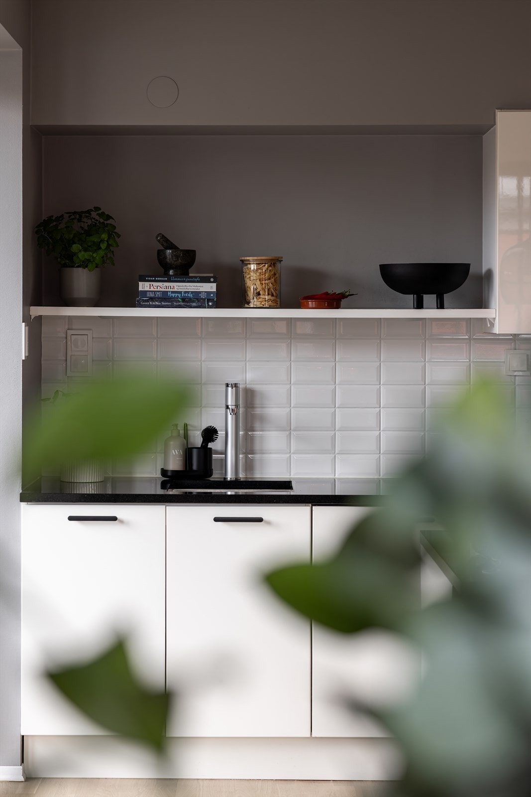 En fin kjøkkenvegg med praktisk hylle og små detaljer som gir varme til rommet. Galleribilde
