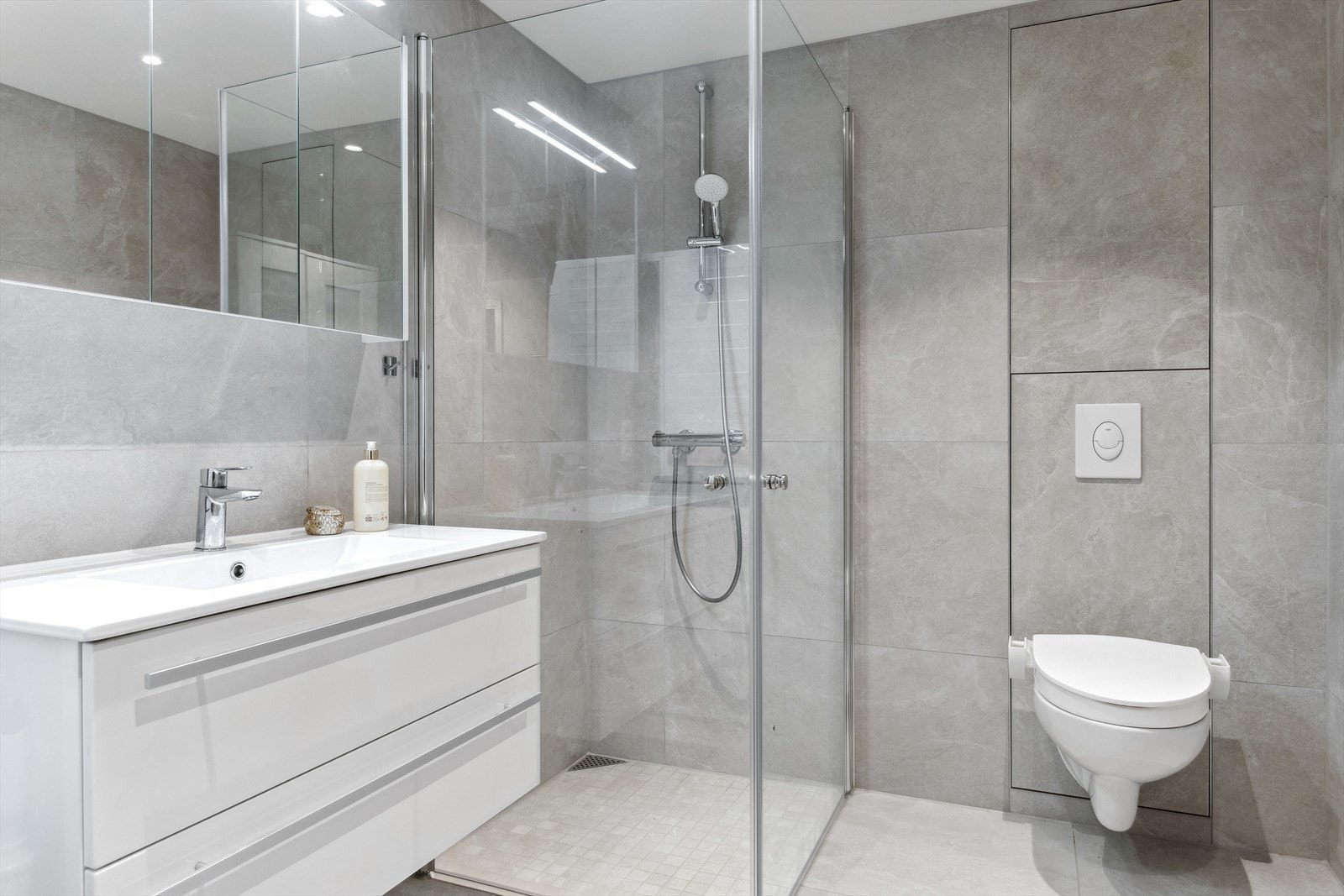 Stilrent bad med store grå fliser på gulv og vegger, samt gulvvarme for ekstra komfort. Galleribilde