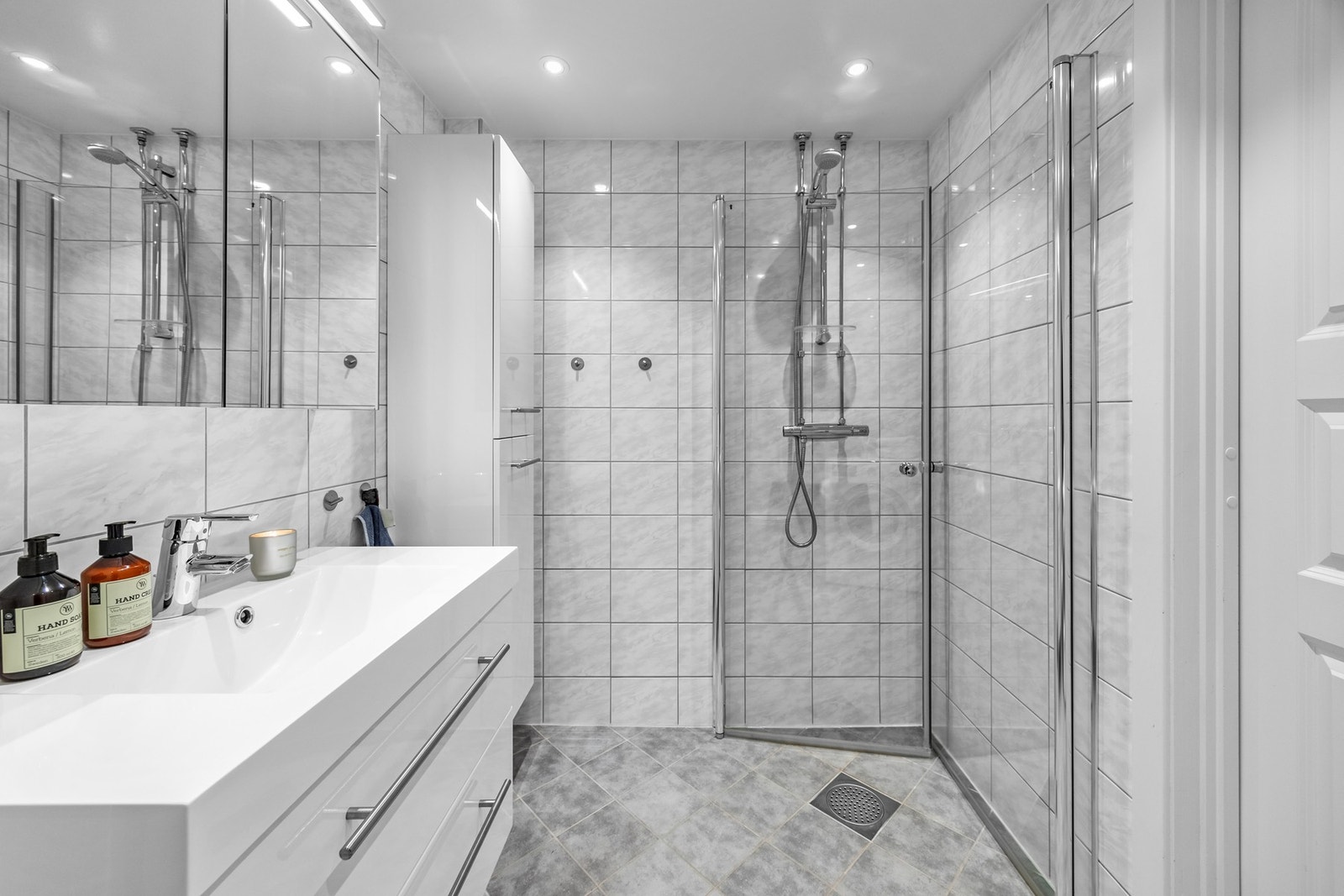 Badet er utstyrt med dusjsone med innfellbare glassdører, vegghengt klosett og bred servantinnredning med vegghengt speil. Opplegg for vaskemaskin. Galleribilde