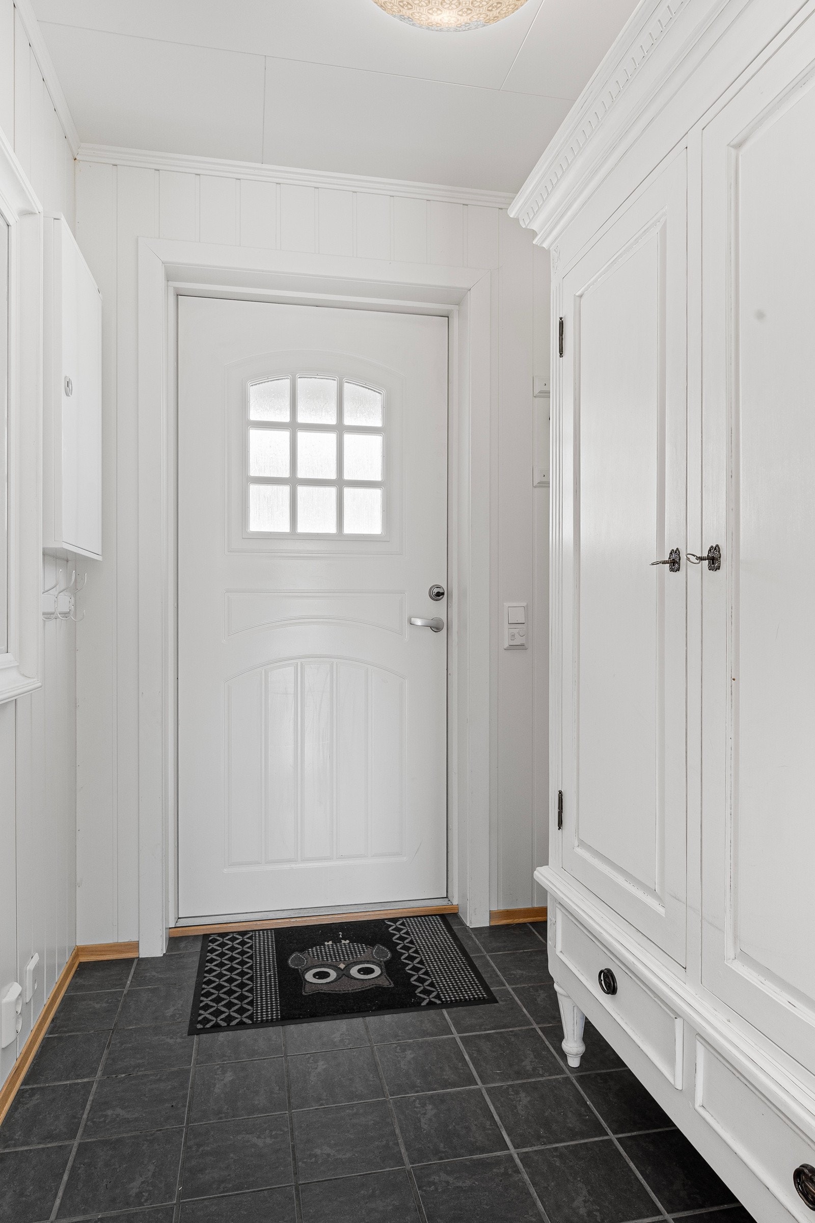 Tiltalende entre med lyse panelplater på vegger og fliser på gulv med gulvvarme som gir et godt førsteinntrykk av boligen. Galleribilde