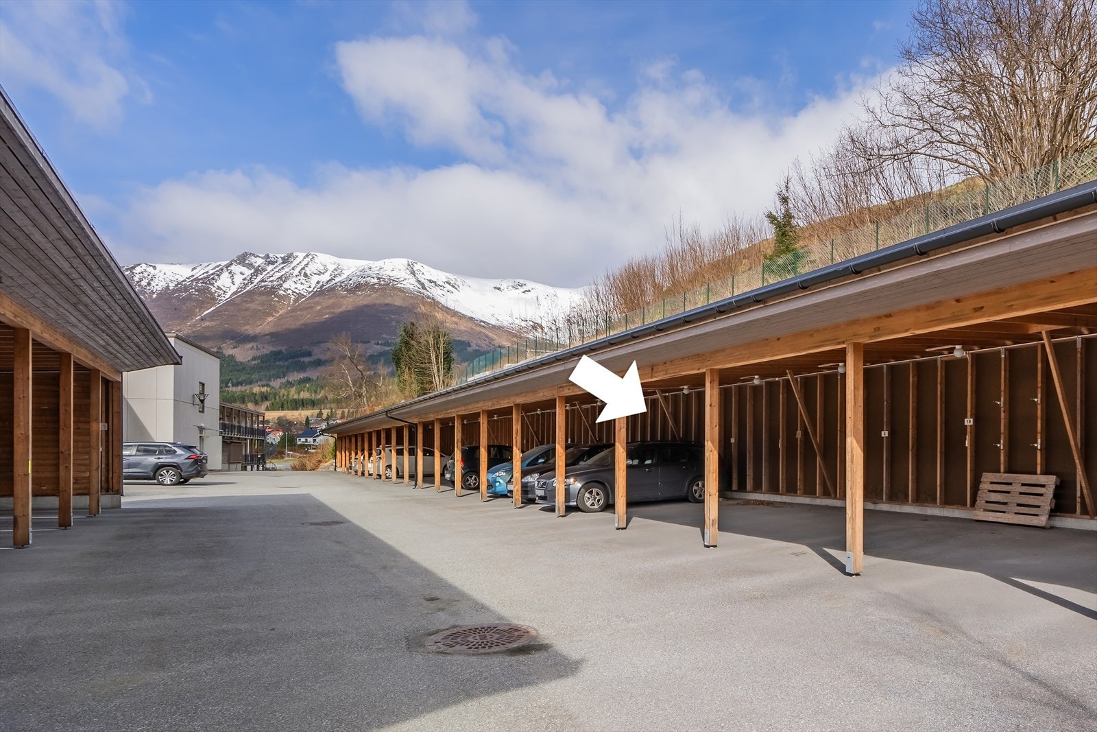 Parkeringsplass for bil i felles carportanlegg. Plass markert med kvit pil Galleribilde