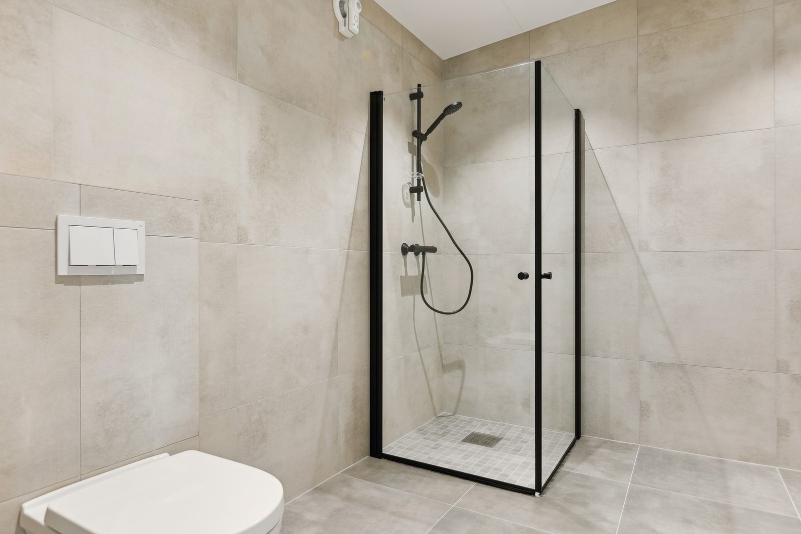 Pent flislagt baderom med moderne innredning og innfellbare dusjdører i glass. Galleribilde