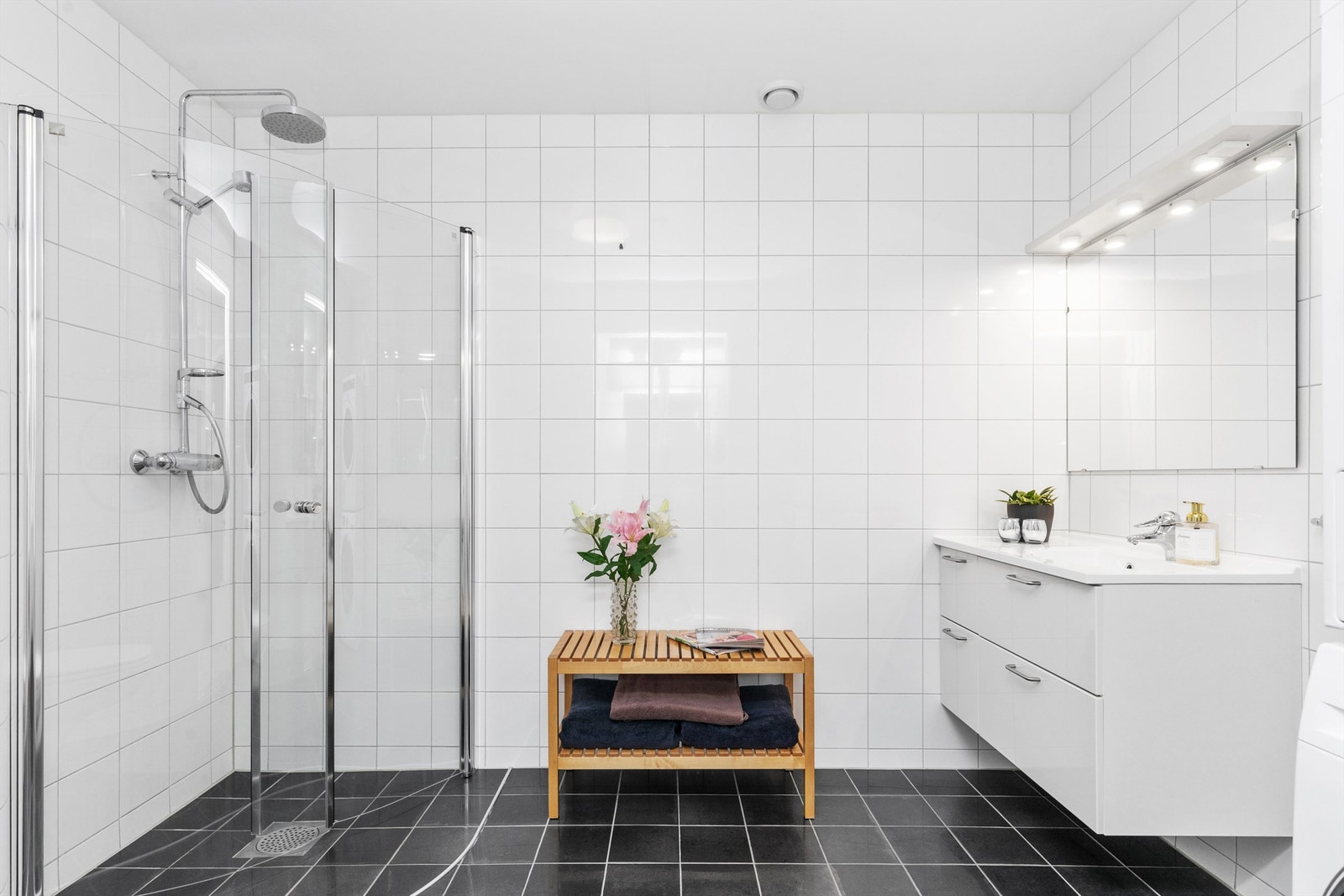 Romslig bad med dusjnisje med glassdører, vegghengt servant med underskuffer og vegghengt toalett. Det er opplegg for vaskemaskin. Galleribilde