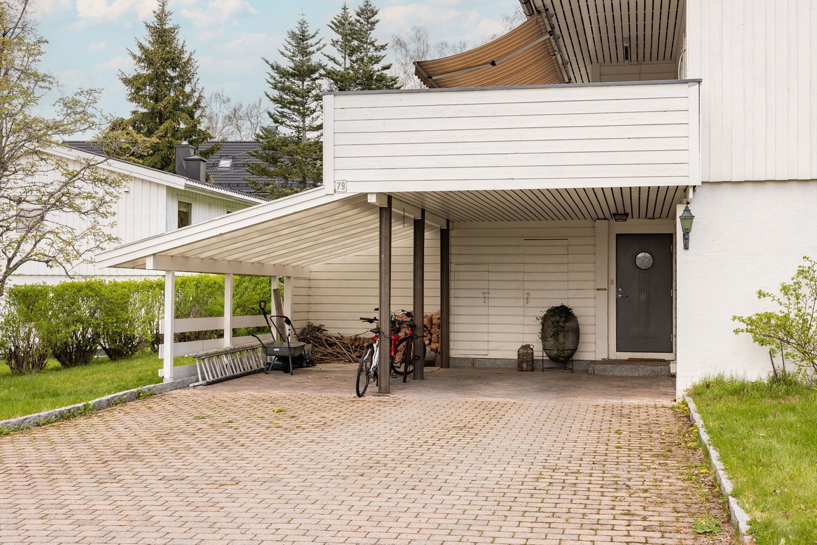 Inngangsparti og carport med plass til to biler og ekstra parkering på egen tomt. I tillegg er det to uteboder innerst i carporten. Galleribilde