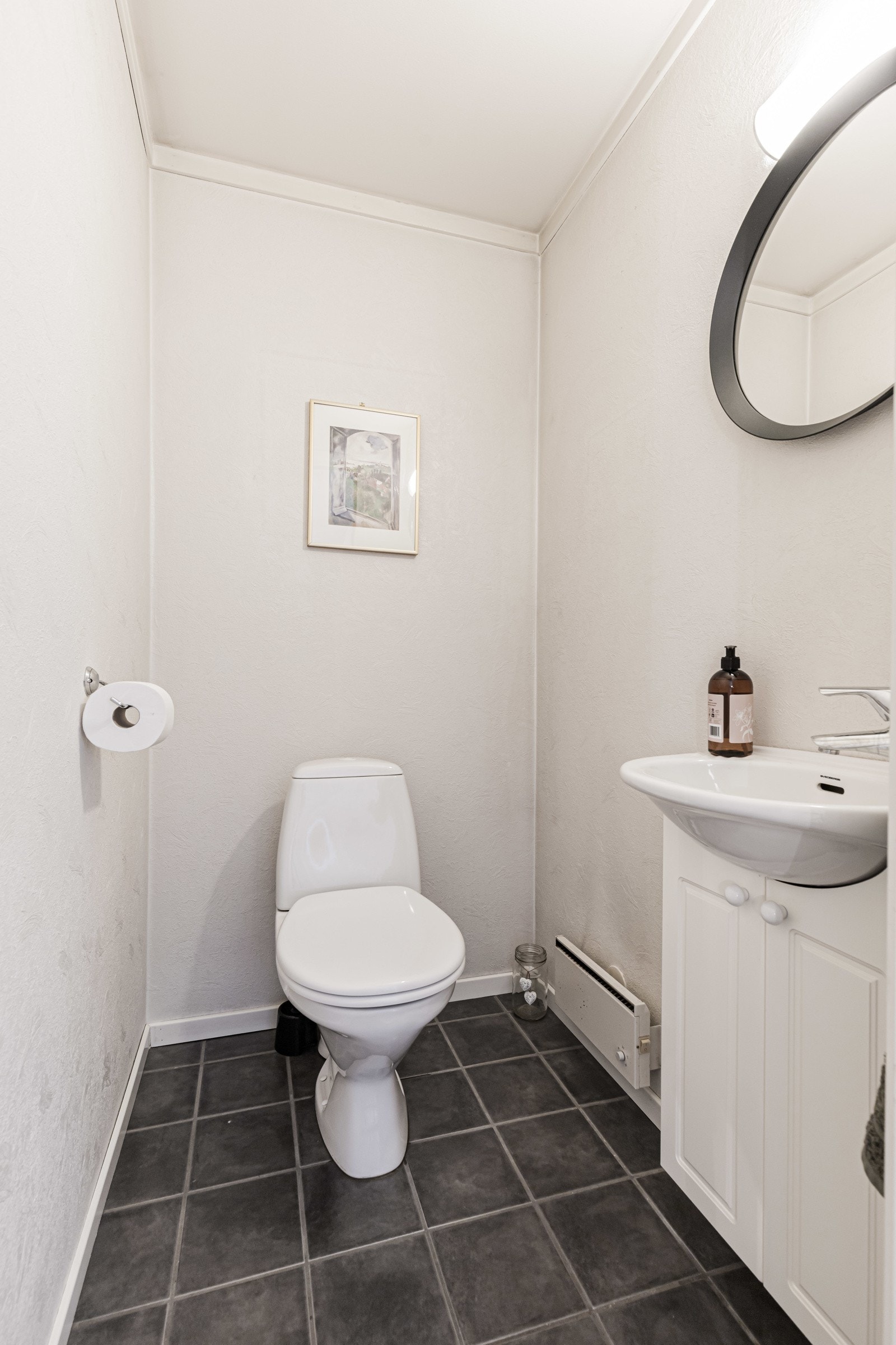Utenom toalettet er wc-rommet innredet med flislagt gulv, hvitt servantskap og speil med tilhørende lys. Galleribilde