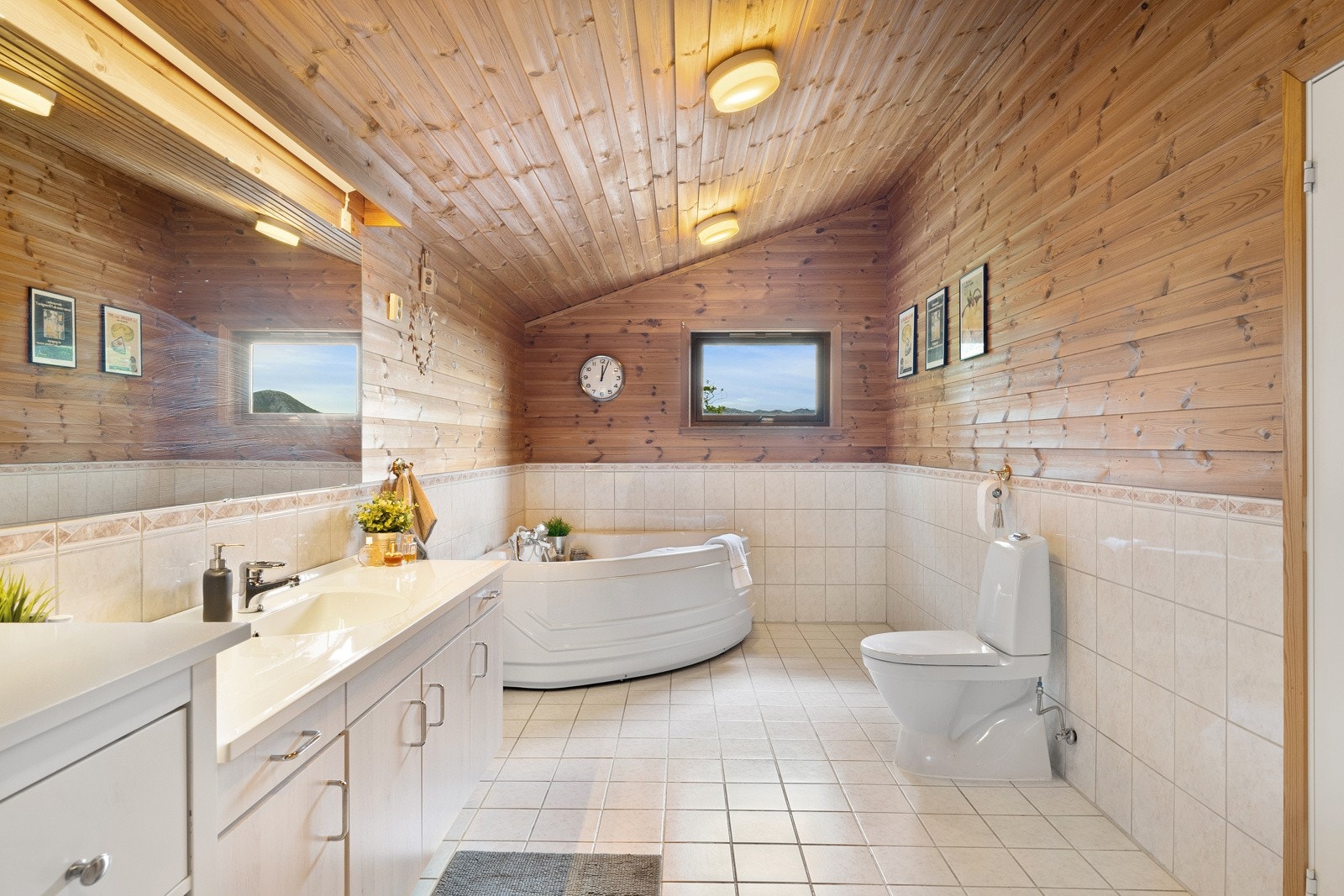 Badet i første etasje har lyse fliser på gulvet med gulvvarme, og veggene har en kombinasjon av lyse fliser og panel. Galleribilde